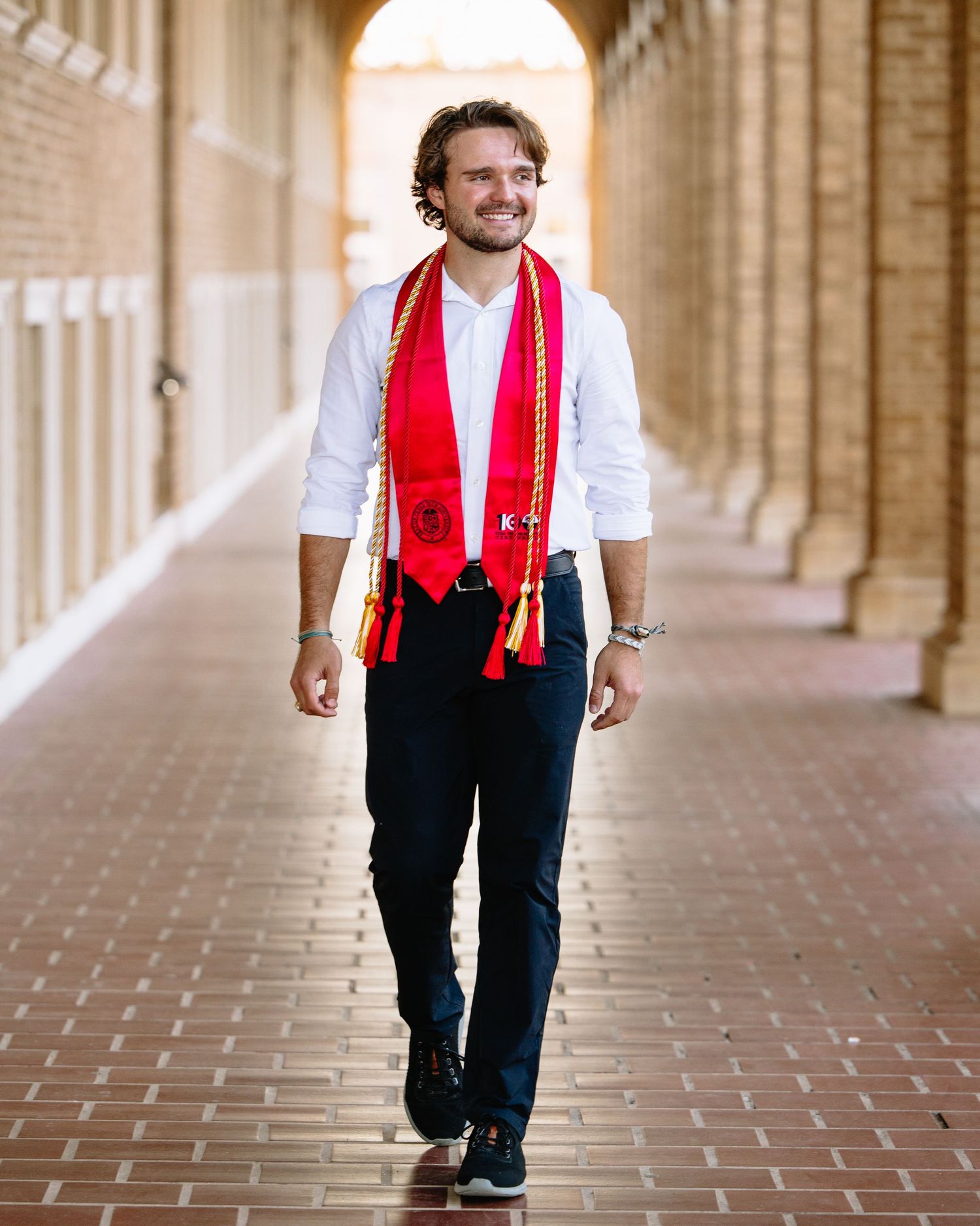 Person wearing a red stole walks confidently through an ornate archway corridor.