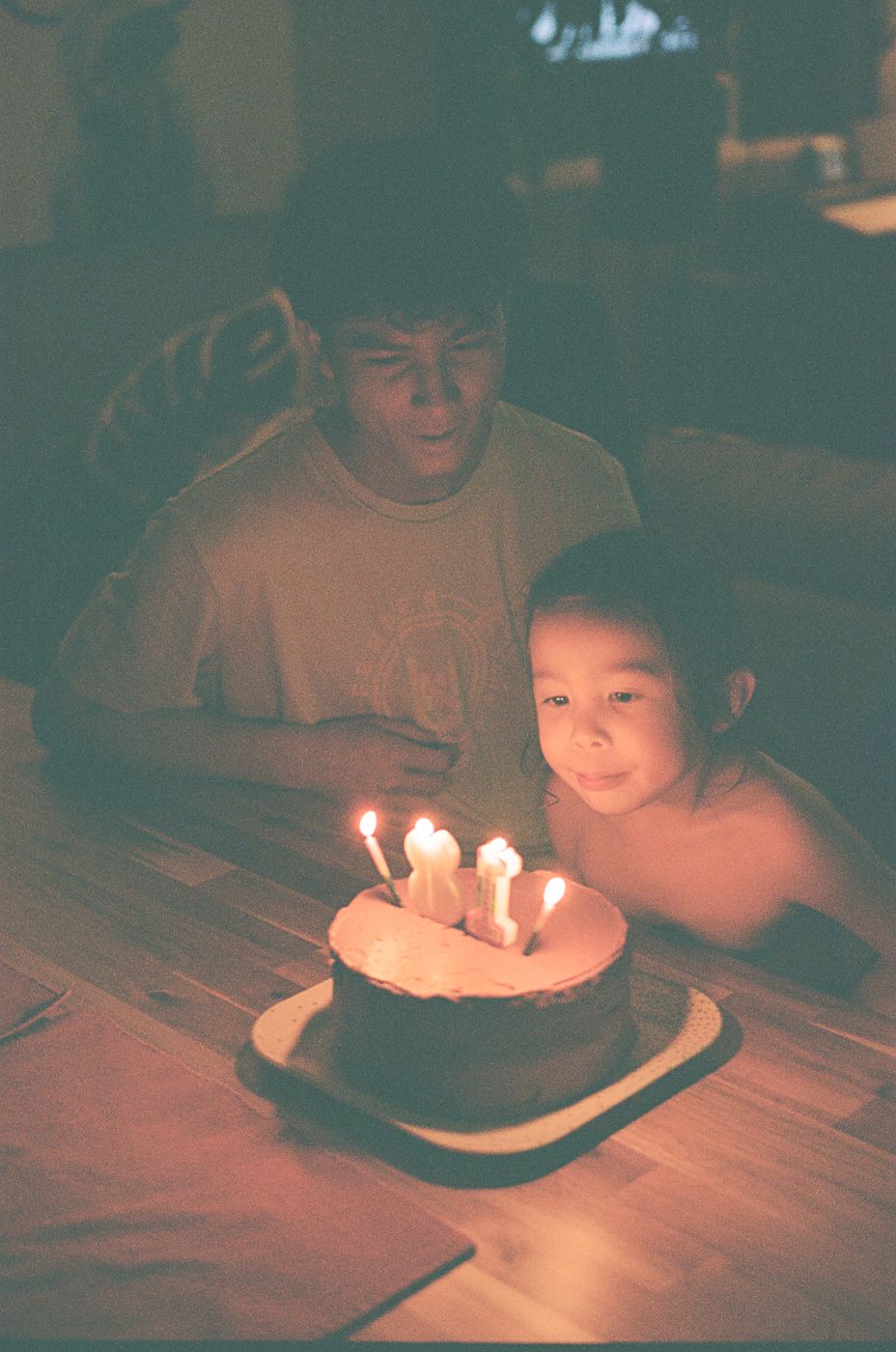 Birthday cake with lit candles on wooden table in atmospheric low lighting.
