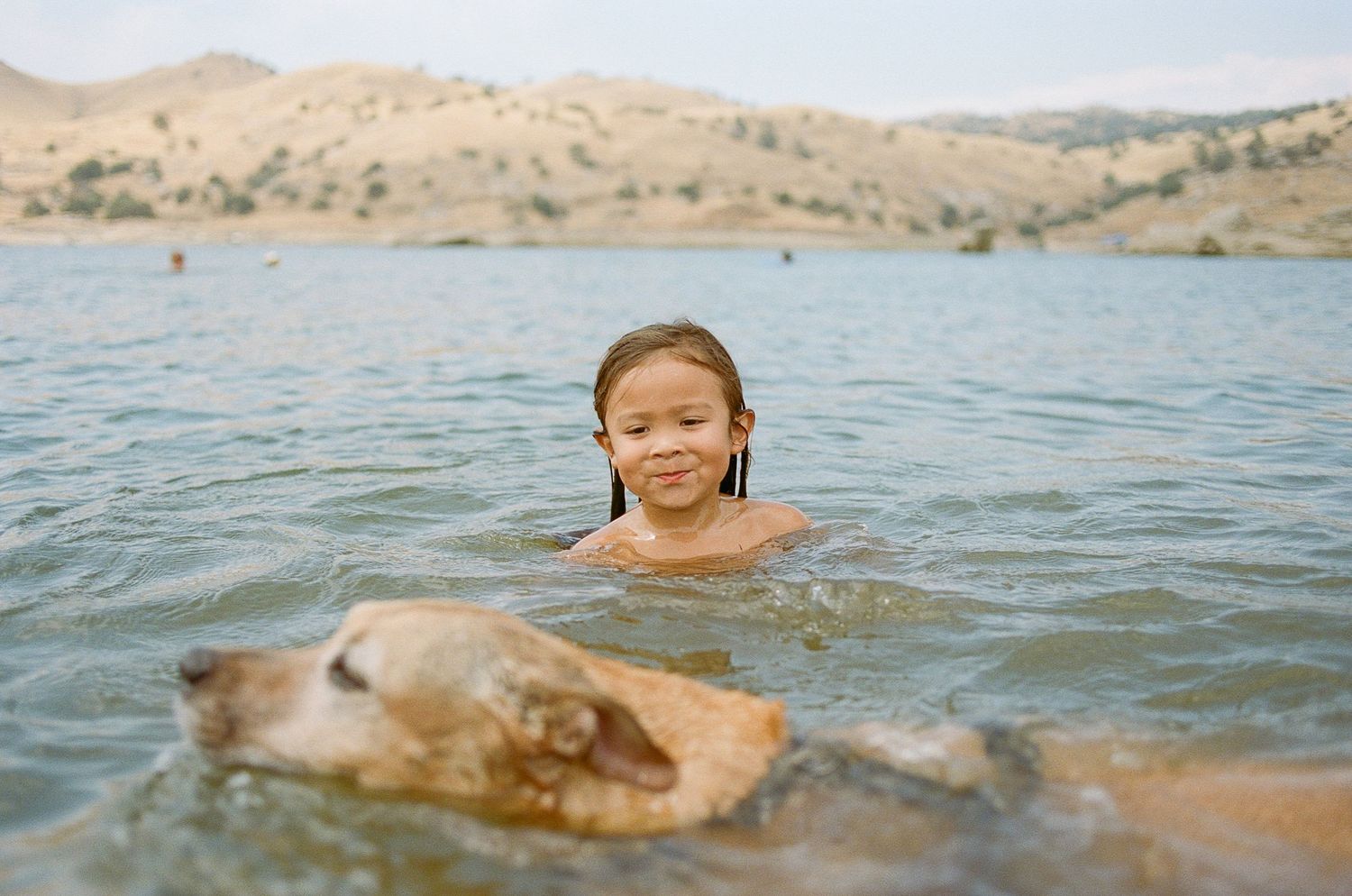 A group of people enjoying a sunny day swimming and playing in a lake surrounded by rolling hills.