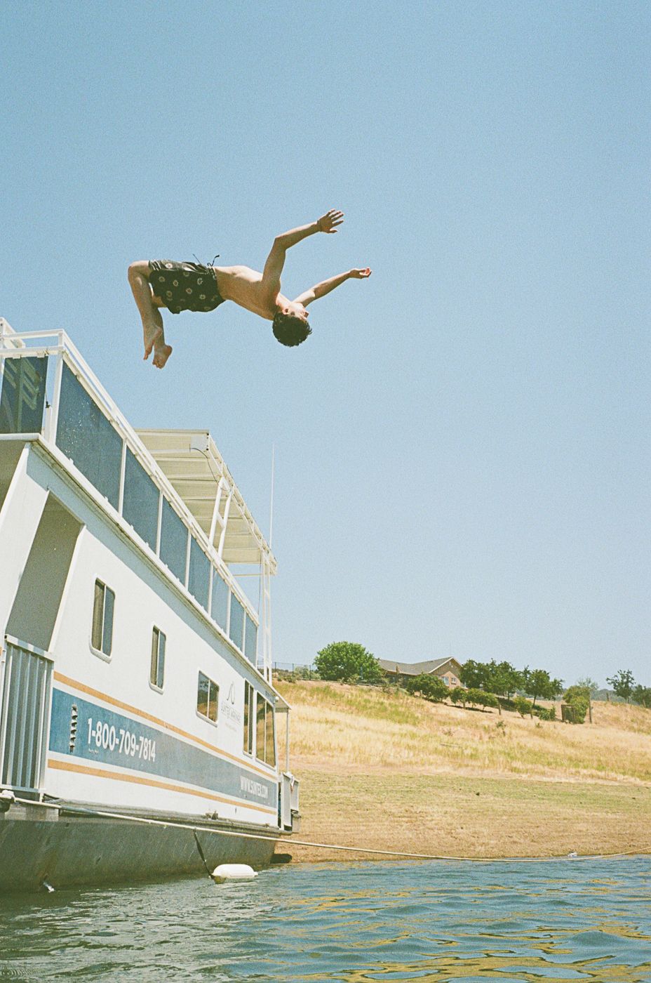 Someone doing a backflip dive off a houseboat into a lake.