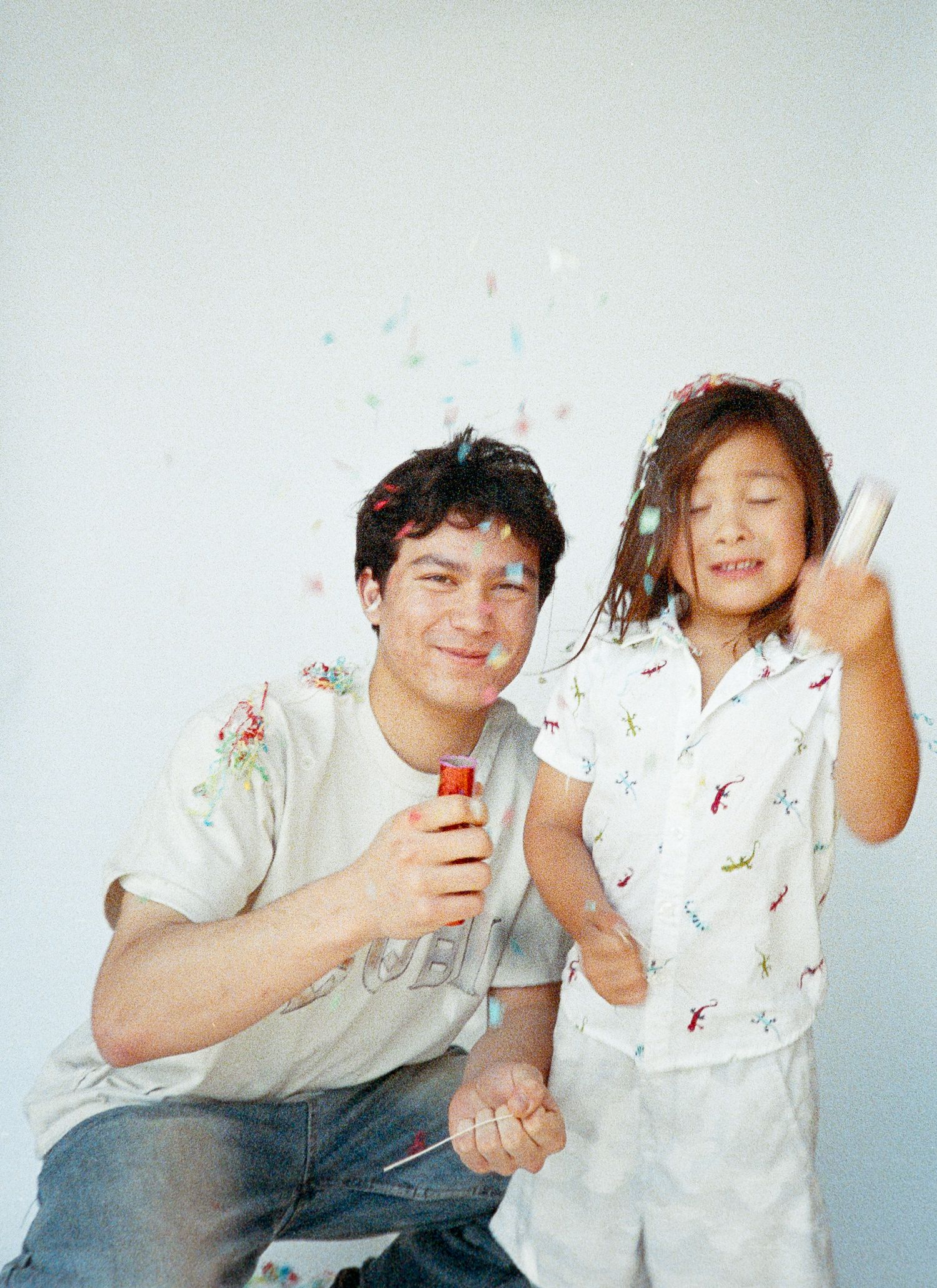 A playful sequence of four photos showing two people in white clothing having fun with confetti against a light background.