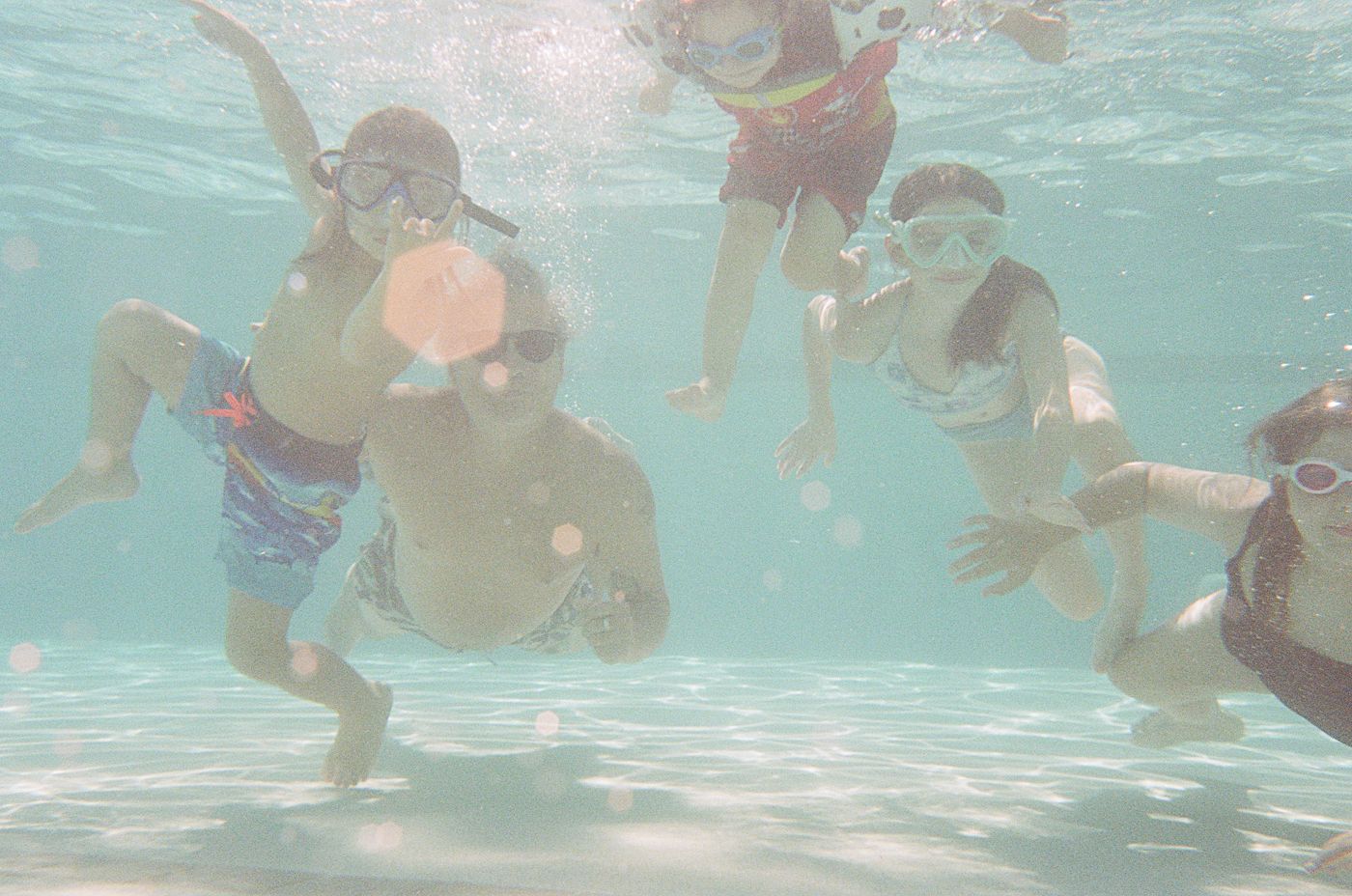 Underwater view of young children swimming in a bright turquoise pool.