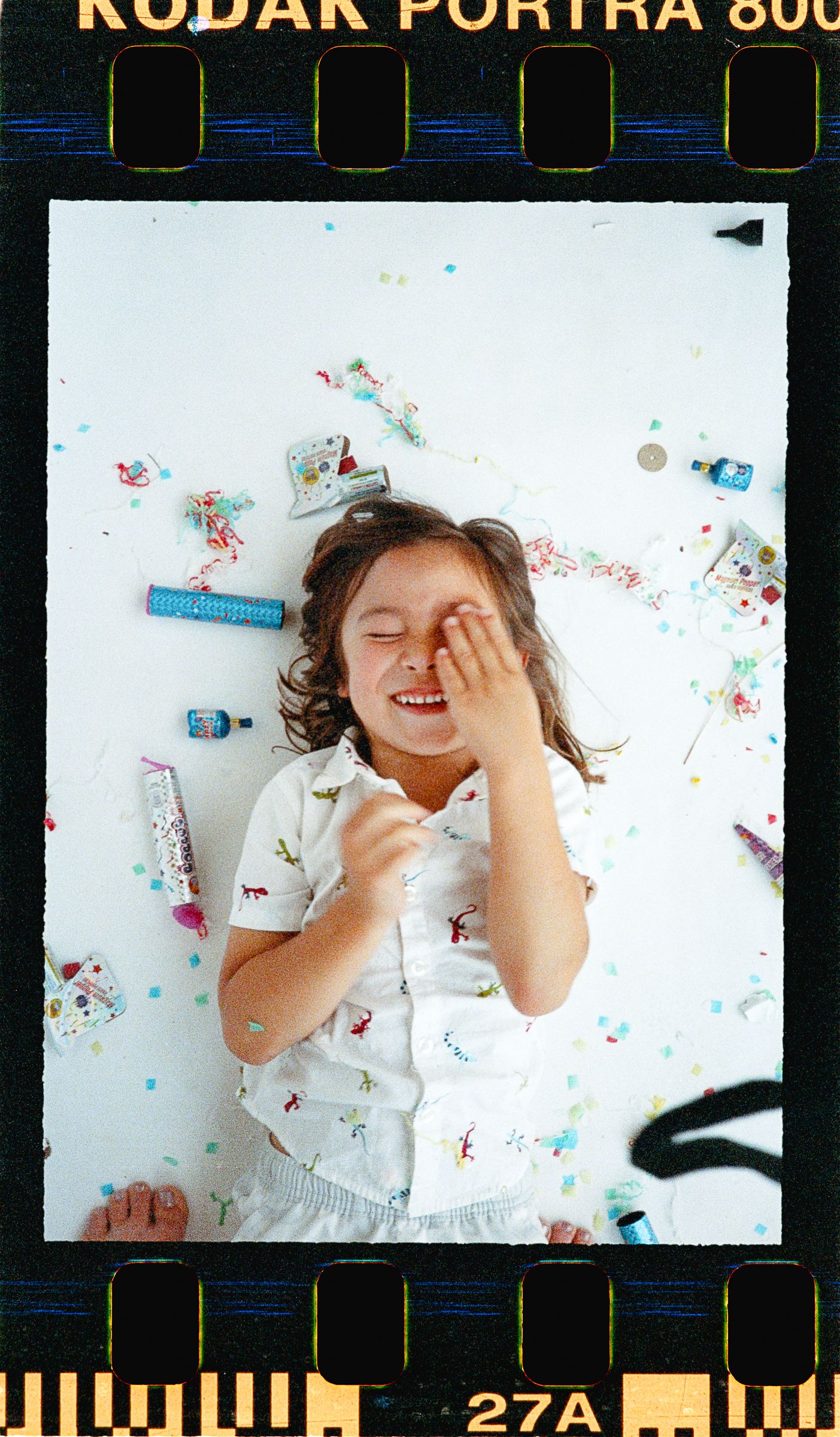 Child laughing on floor surrounded by confetti and toys, shot on Kodak Portra 800 film.