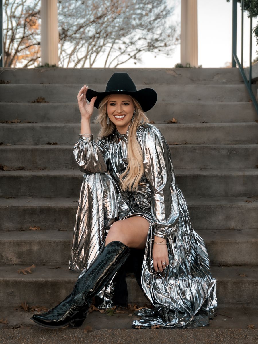 Stylish western look with silver metallic dress, black hat and boots on outdoor staircase.