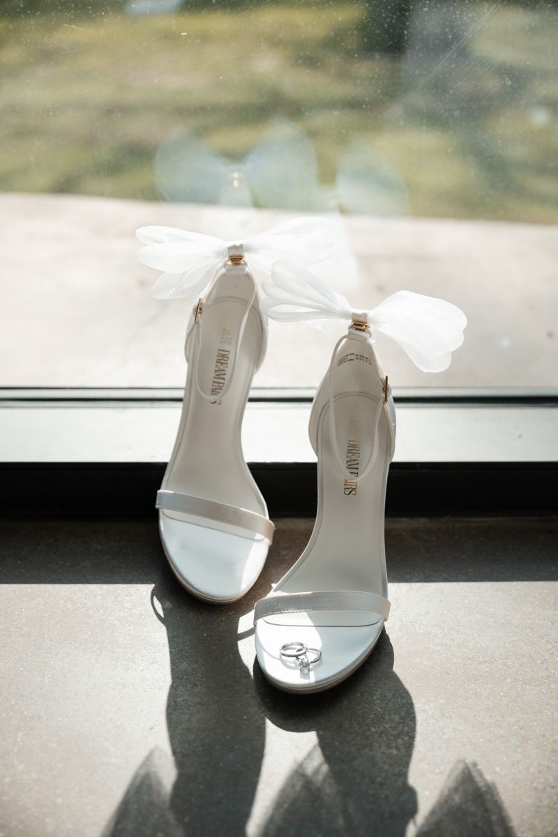 White bridal heels with delicate bow details photographed on windowsill.