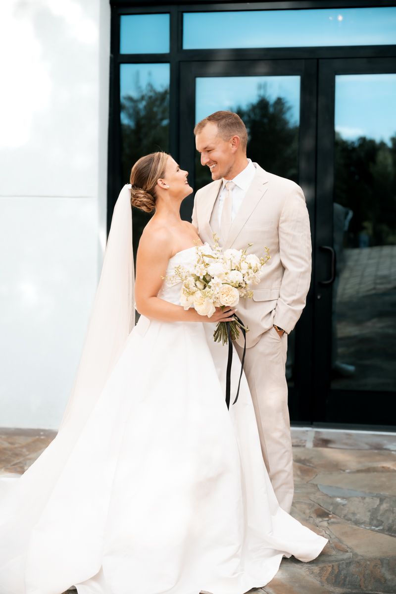 Romantic wedding portrait in front of modern glass building entrance.