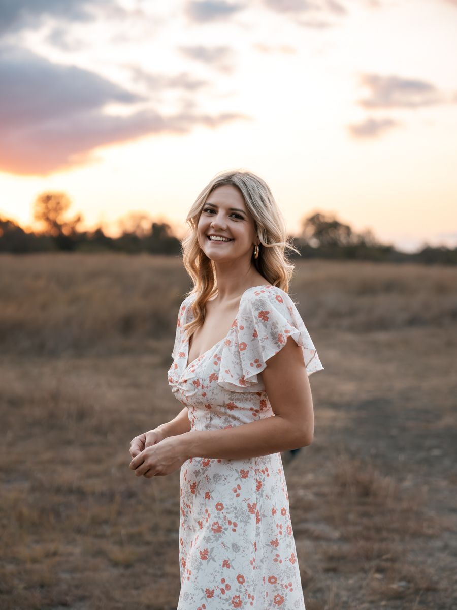 Floral sundress captured in golden sunset light in rustic field setting.