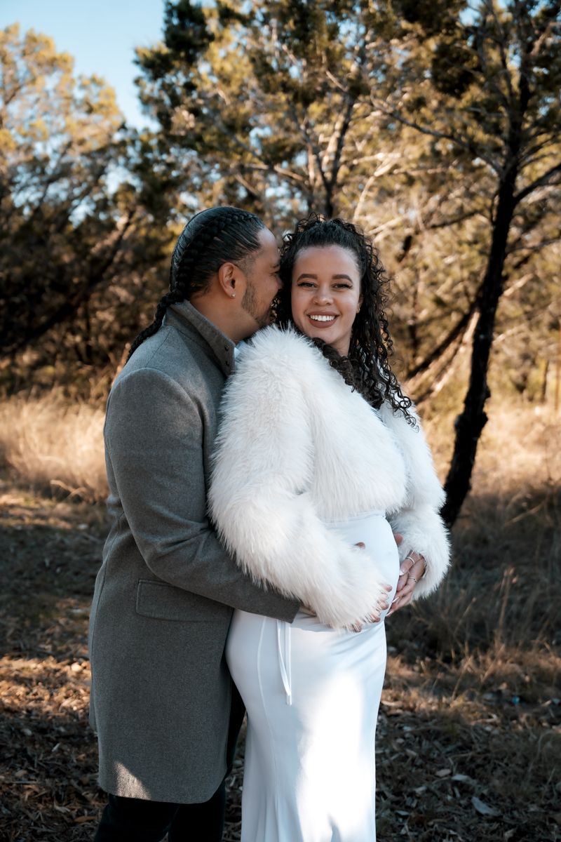 Romantic maternity photo of a couple embracing outdoors in autumn scenery.