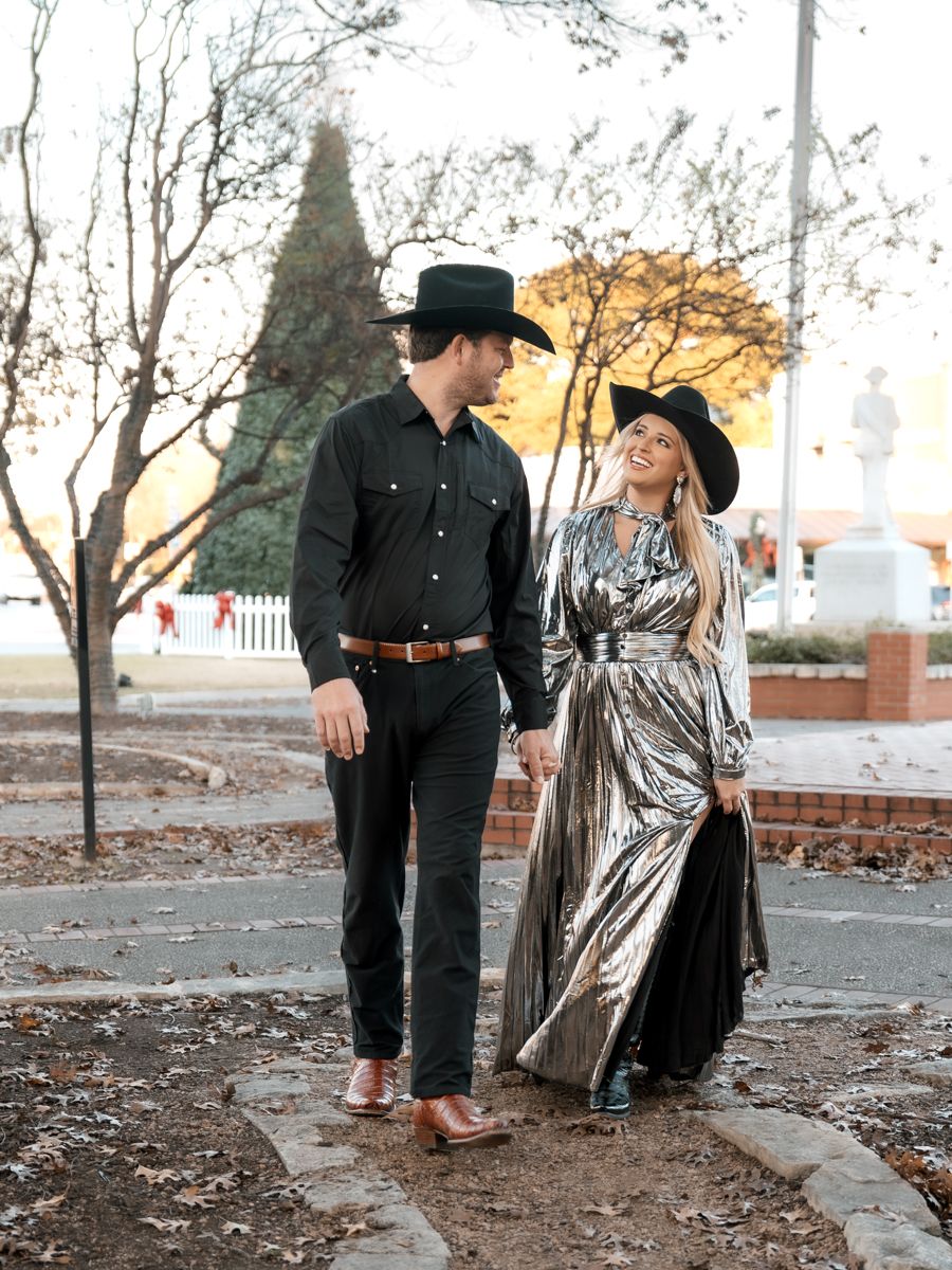 Couple in western wear walks along path, woman wearing striking metallic dress.