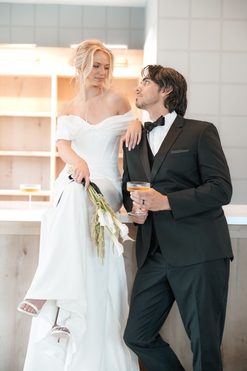 Modern wedding couple in black and white attire pose casually with cocktails.