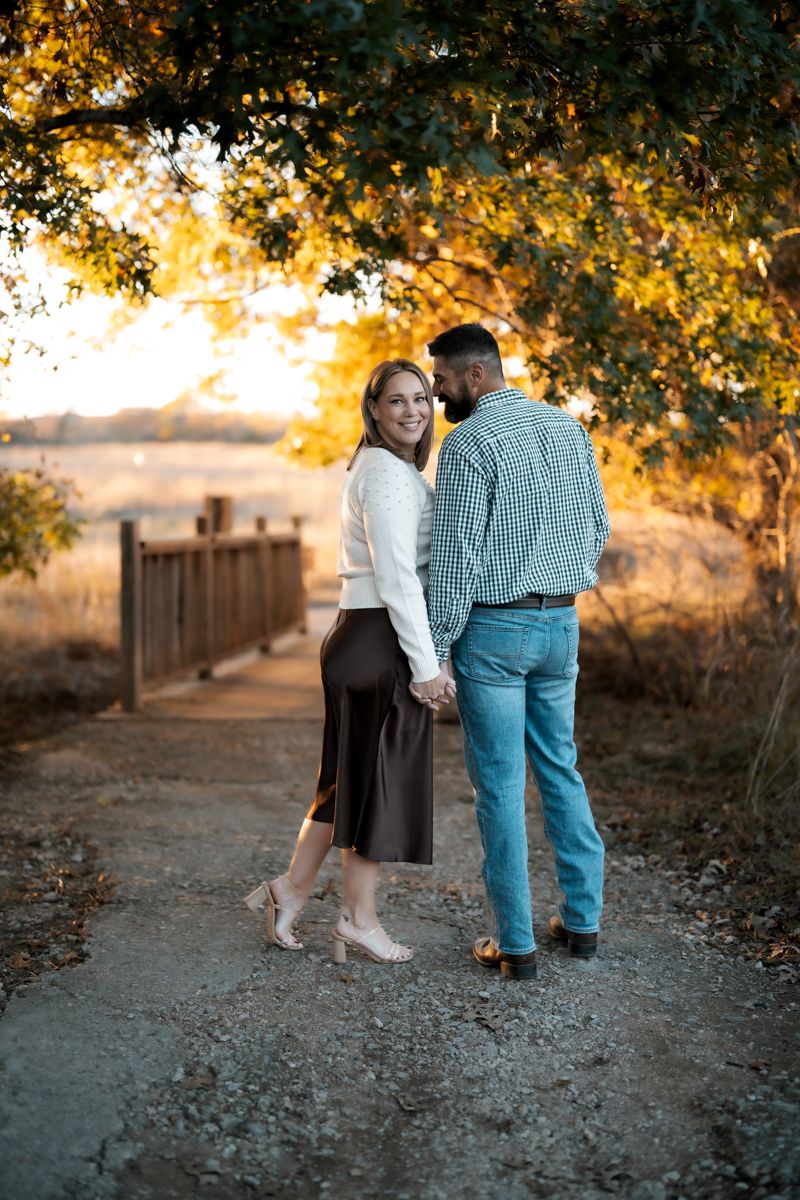 A romantic sunset portrait of a couple on a rustic path beneath golden autumn trees.