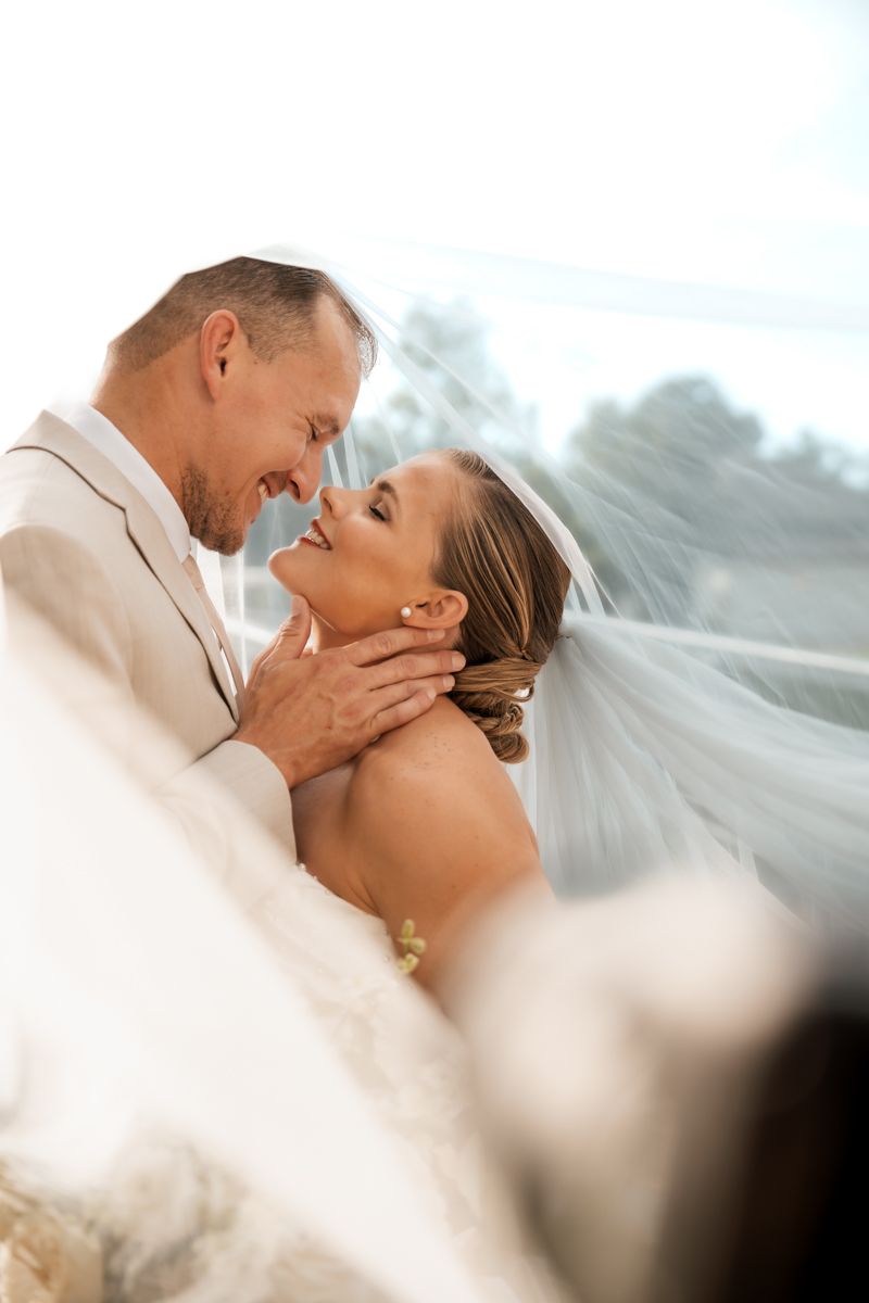 Romantic wedding moment captured as newlyweds share an intimate embrace with flowing veil in soft lighting.