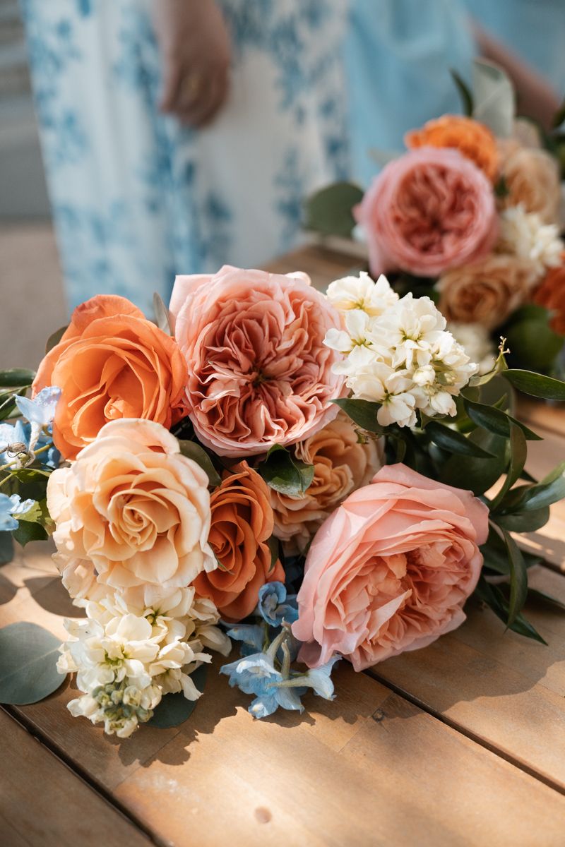 A lush bridal bouquet with coral, peach and white roses accented with delicate blue flowers.