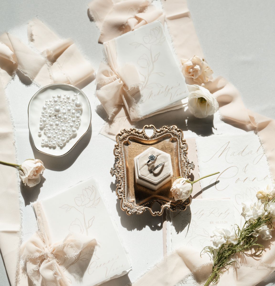 Elegant wedding details with vintage frame, pearls, and delicate blush ribbons on white textured surface.