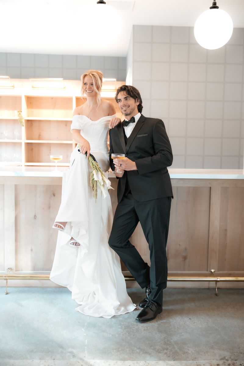 A classic wedding photo featuring a couple in traditional white gown and black tuxedo posed against a modern interior.