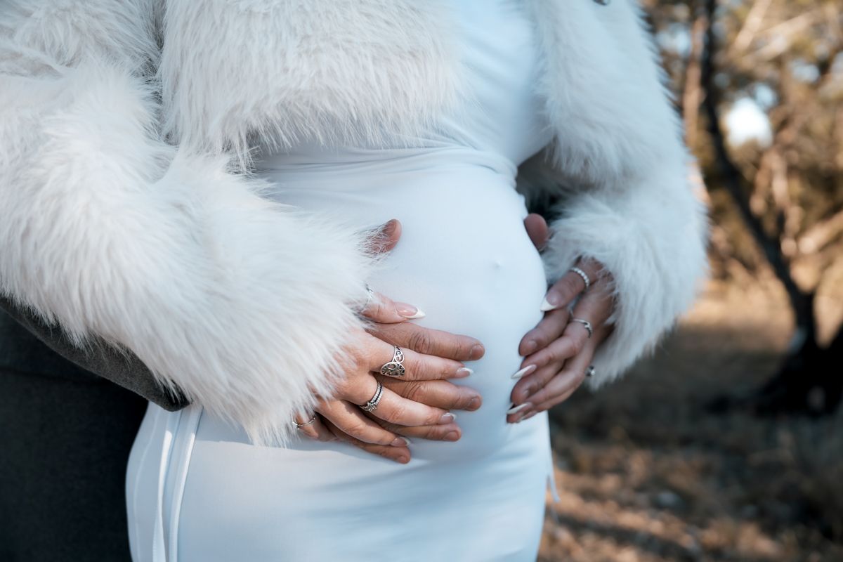Close-up of a pregnant woman in a white dress with a luxurious white fur coat.