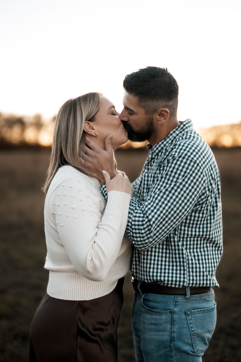 A tender romantic moment between a couple sharing a kiss in an outdoor setting during golden hour.