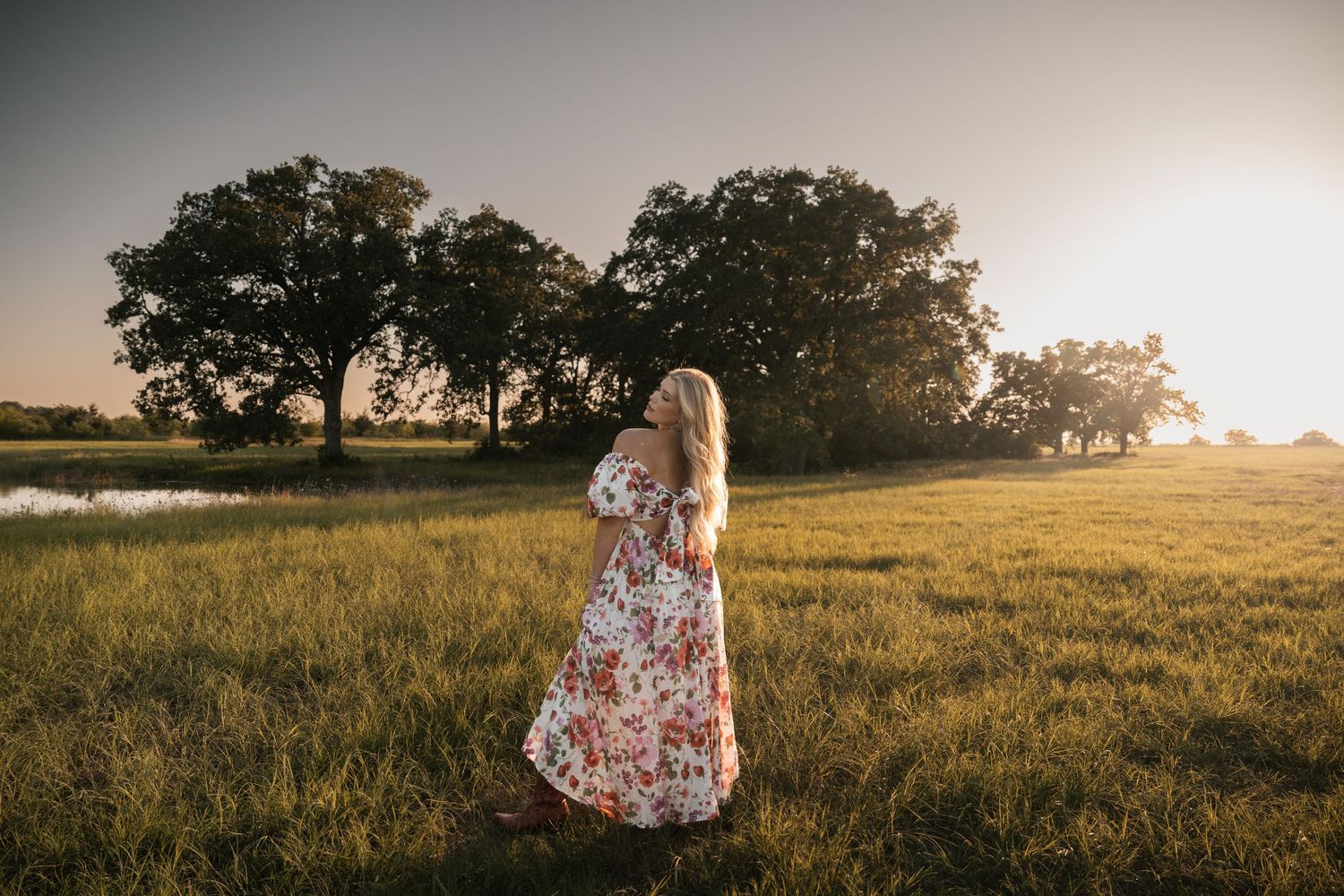 Dreamy sunset photo of floral dress silhouette in open field with trees.