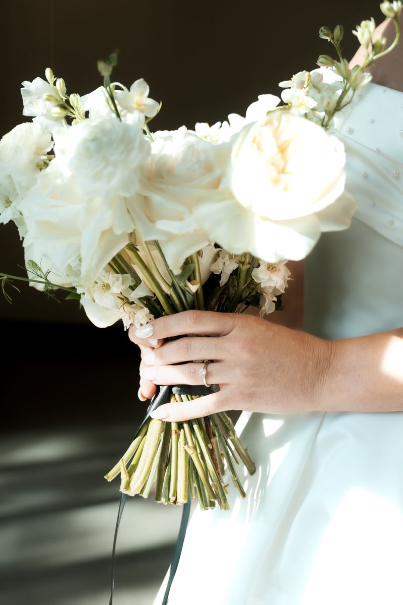 Close-up of white wedding bouquet with roses and delicate flowers tied with ribbon.
