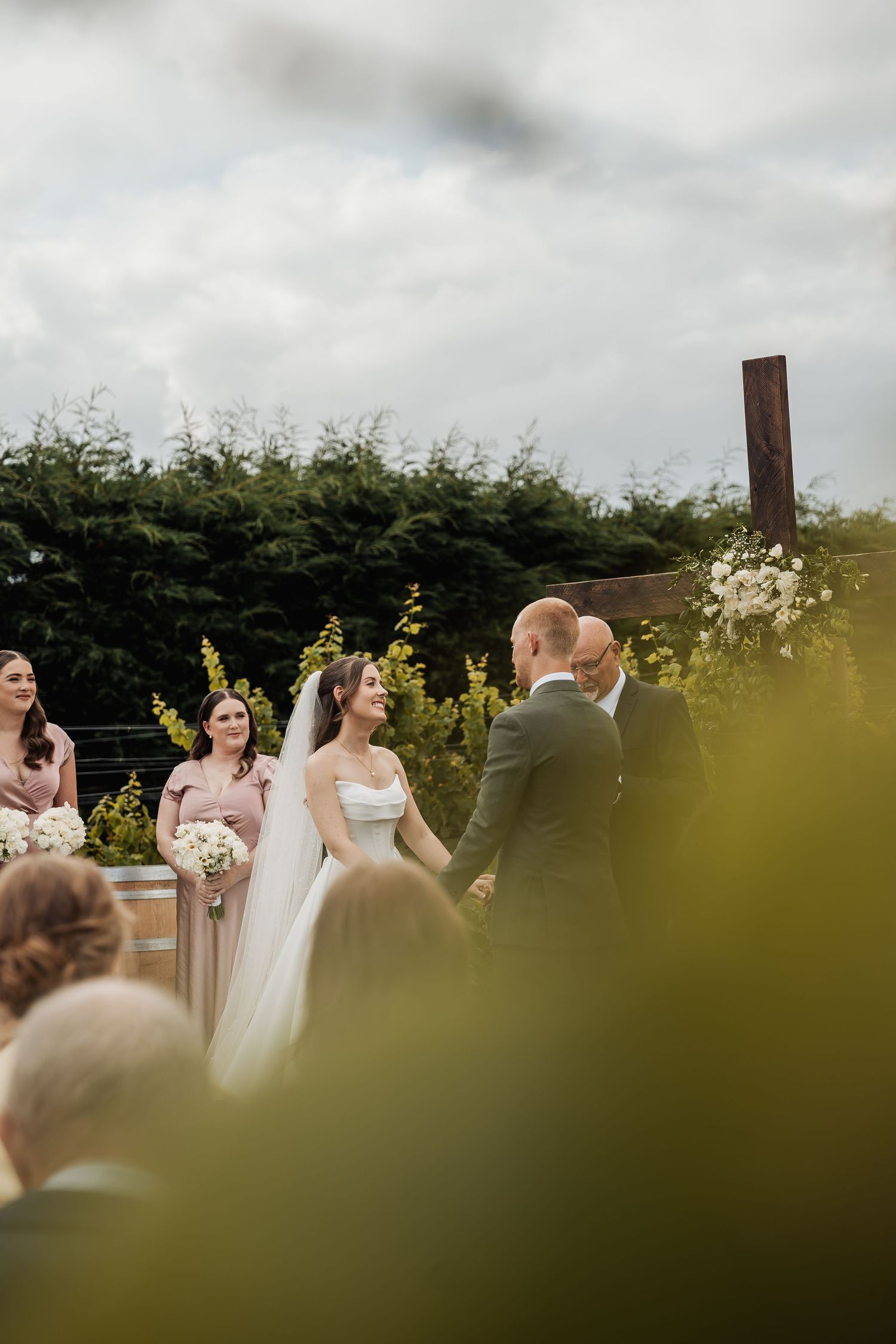 Bride and groom holding hands at an outdoor wedding ceremony with bridesmaids in pink dresses nearby.