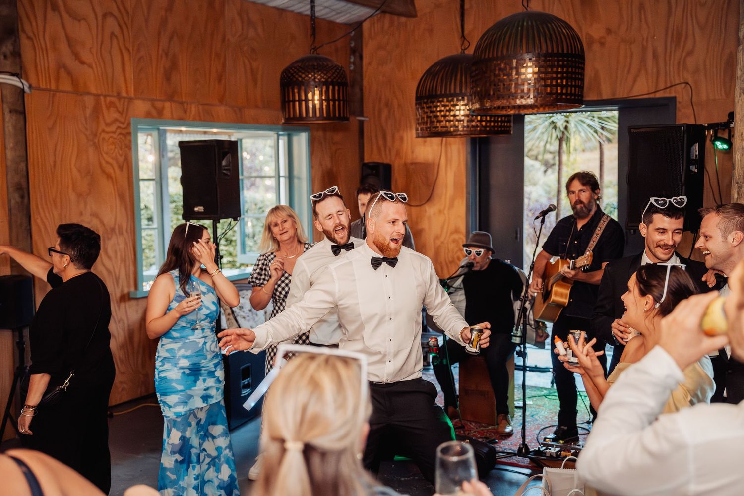 Groom in white shirt dancing energetically with wedding guests at lively indoor reception with live band.