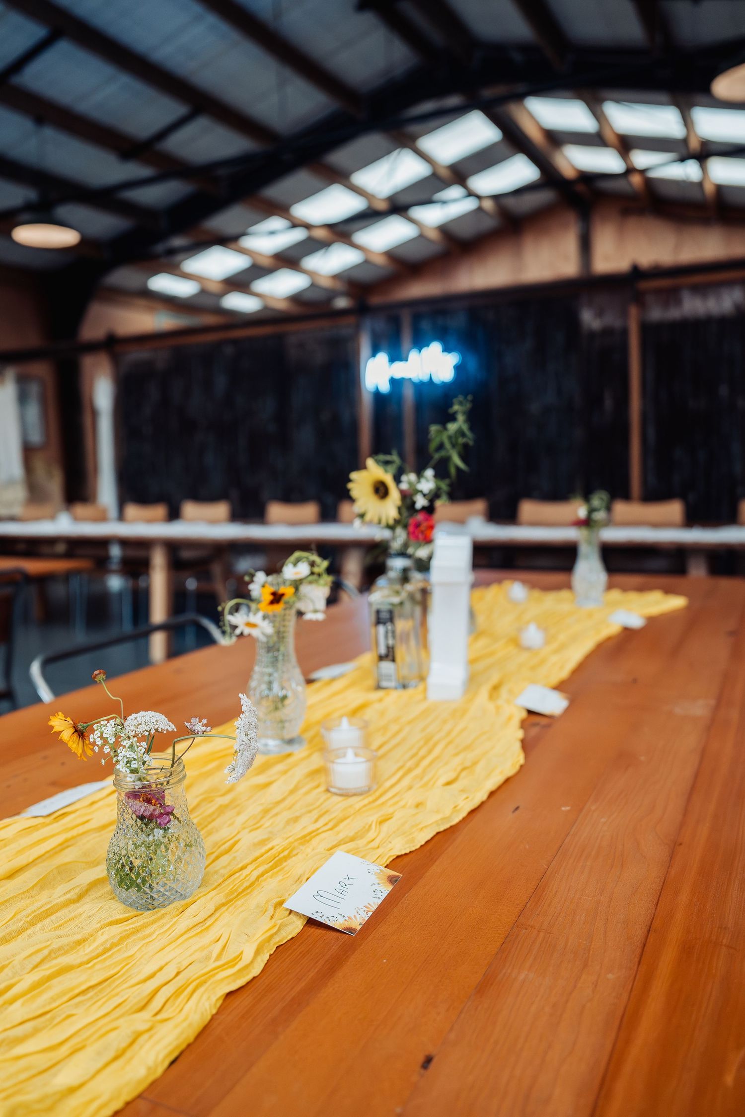 Yellow table runner with wildflower centerpieces decorating a wooden wedding reception table.