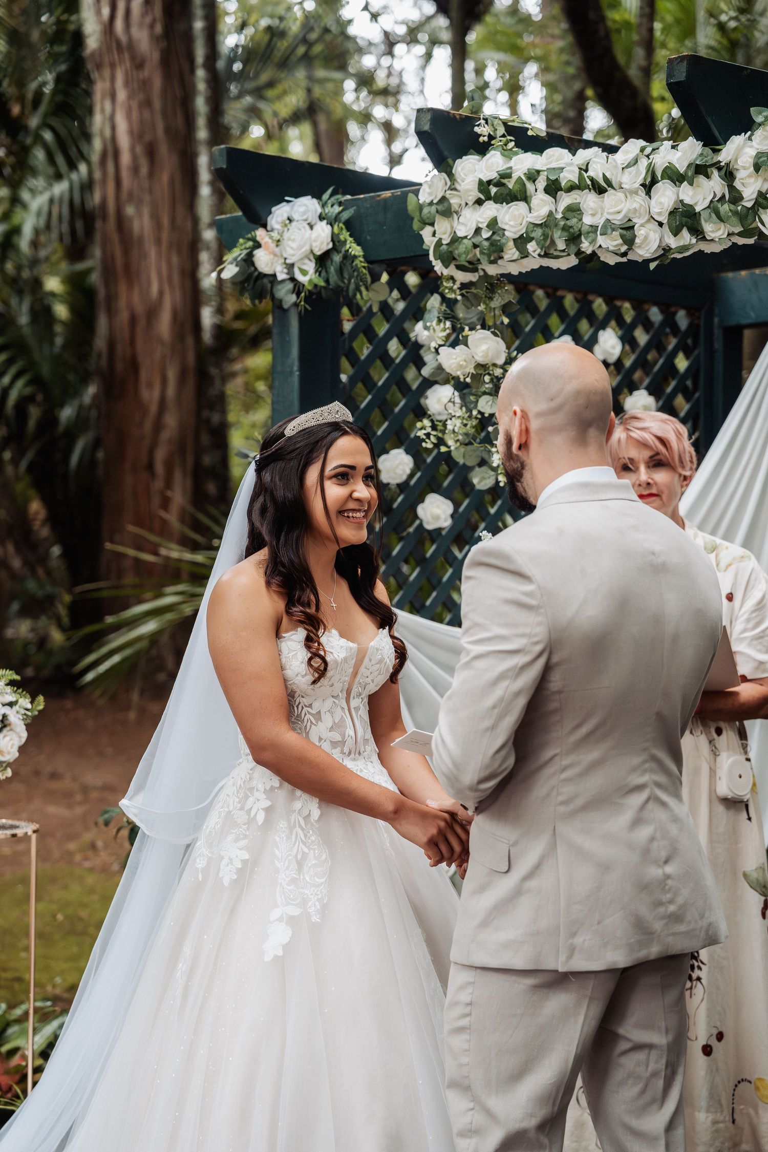 Bride and groom holding hands at outdoor wedding ceremony under floral arch.