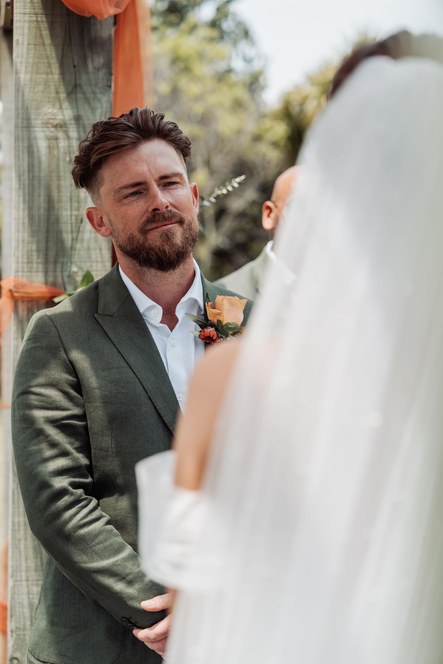 Emotional groom in green suit gazing at bride during outdoor wedding ceremony at the altar.