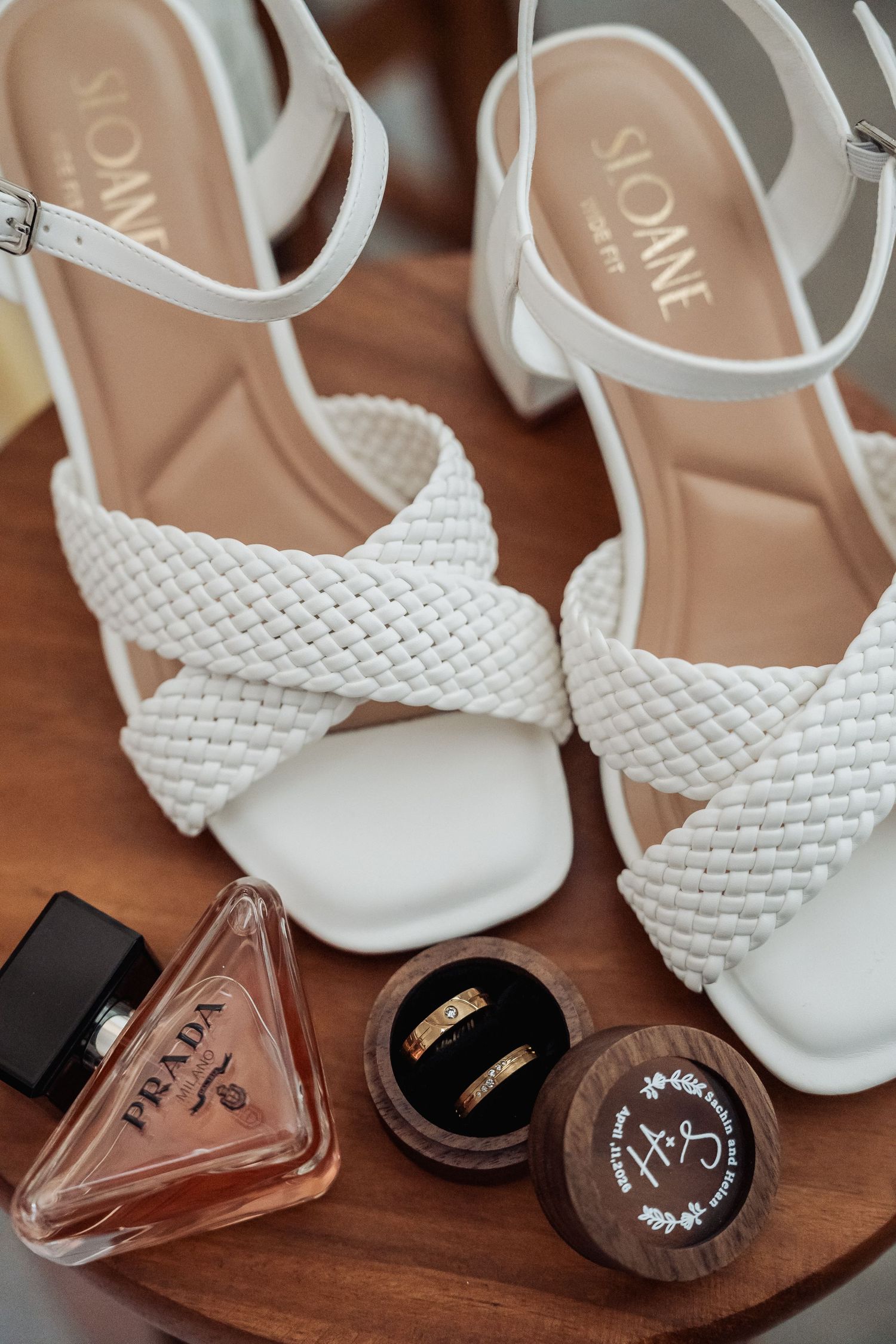 White braided block heel sandals by Sloane displayed with Prada perfume and gold wedding bands in wooden ring box.
