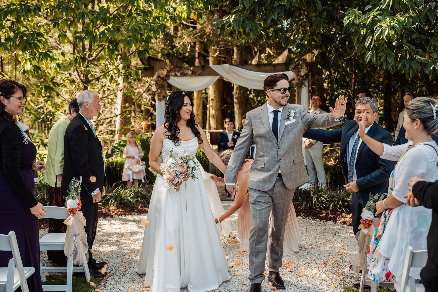 Bride and groom celebrate walking down the aisle at an outdoor garden wedding ceremony surrounded by guests.