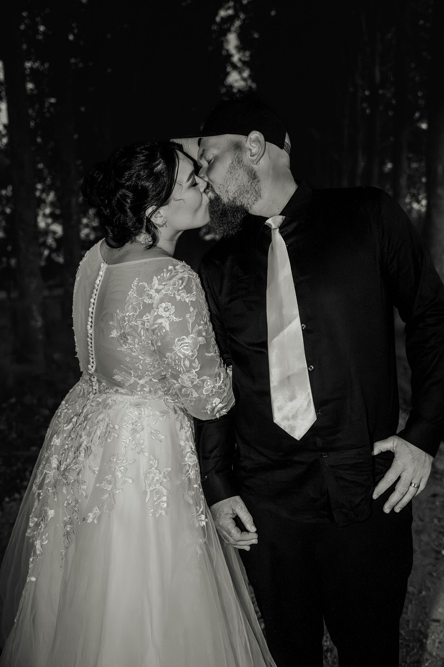 A tender black and white photo capturing an intimate wedding moment in a forest setting.