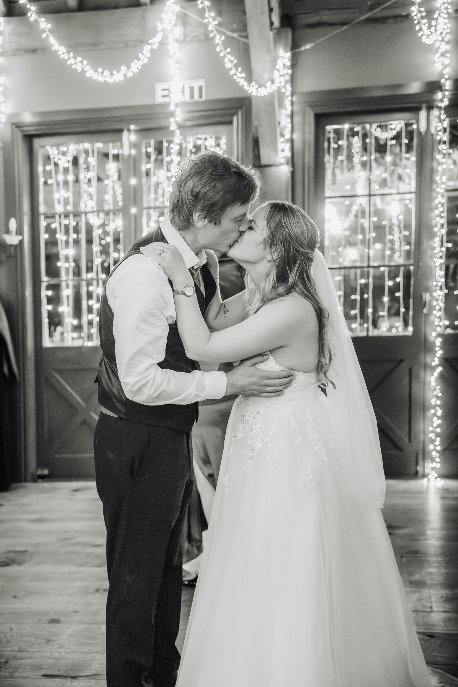 A romantic black and white wedding photo shows a couple sharing their first dance surrounded by twinkling string lights.