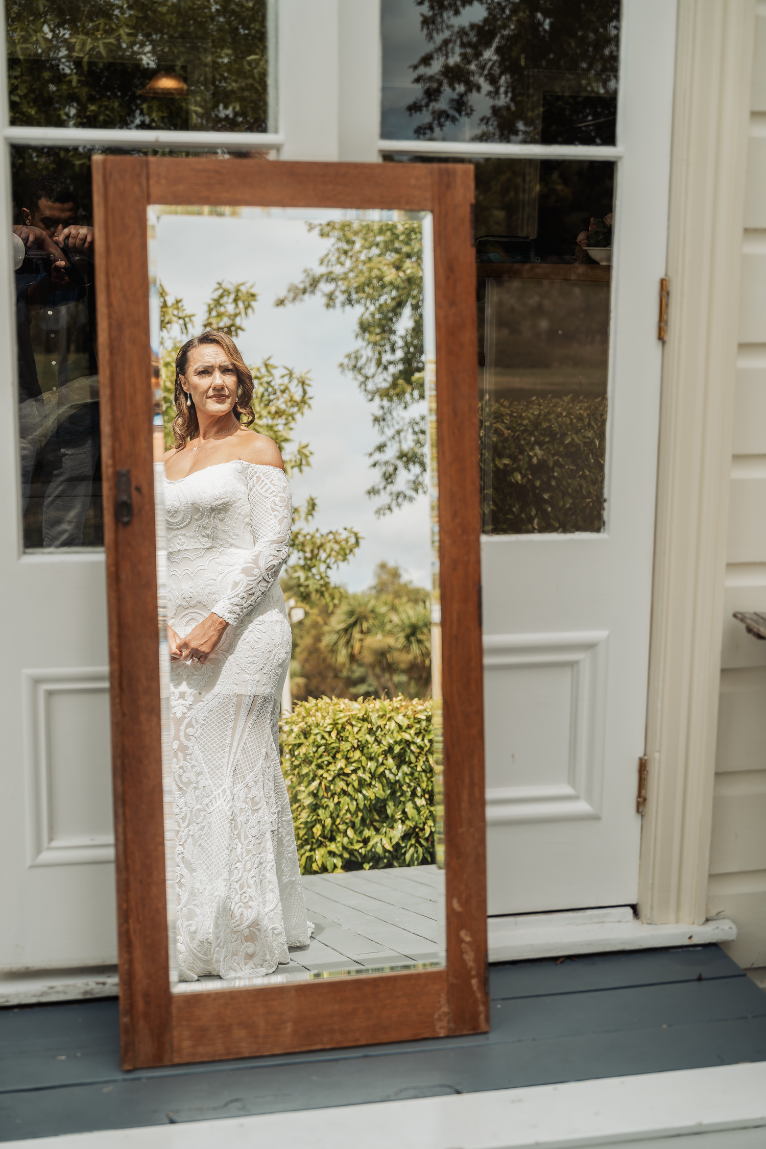 Mirror reflection shows elegant lace wedding dress in natural outdoor setting.