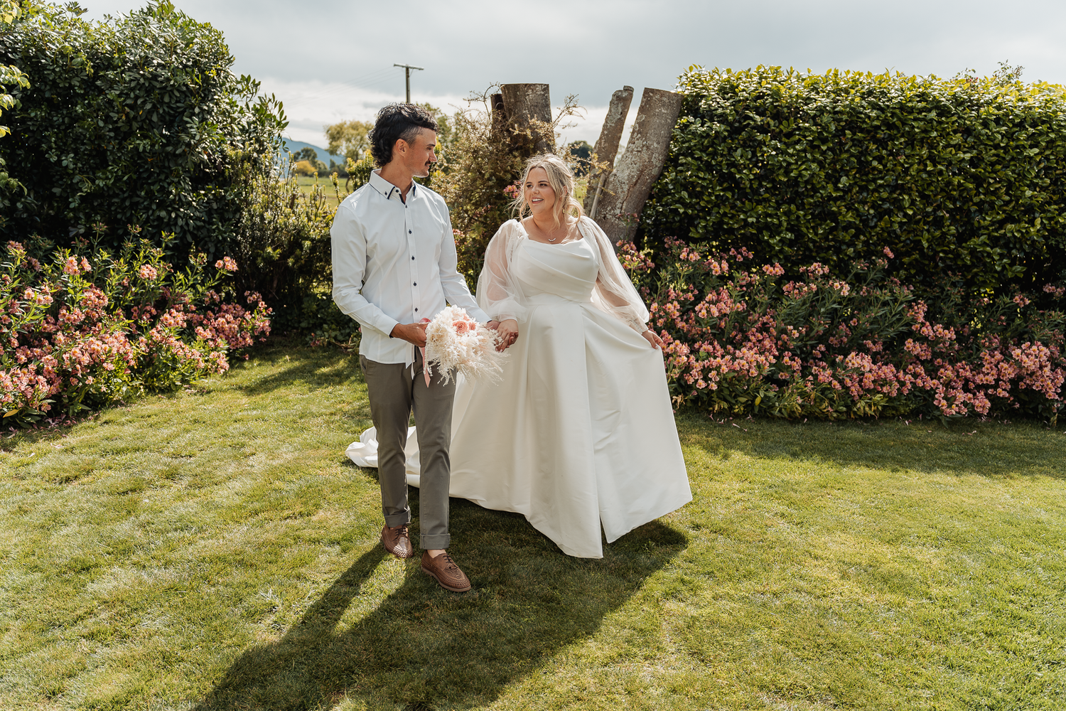 A joyful couple walks hand in hand through a garden on their wedding day.