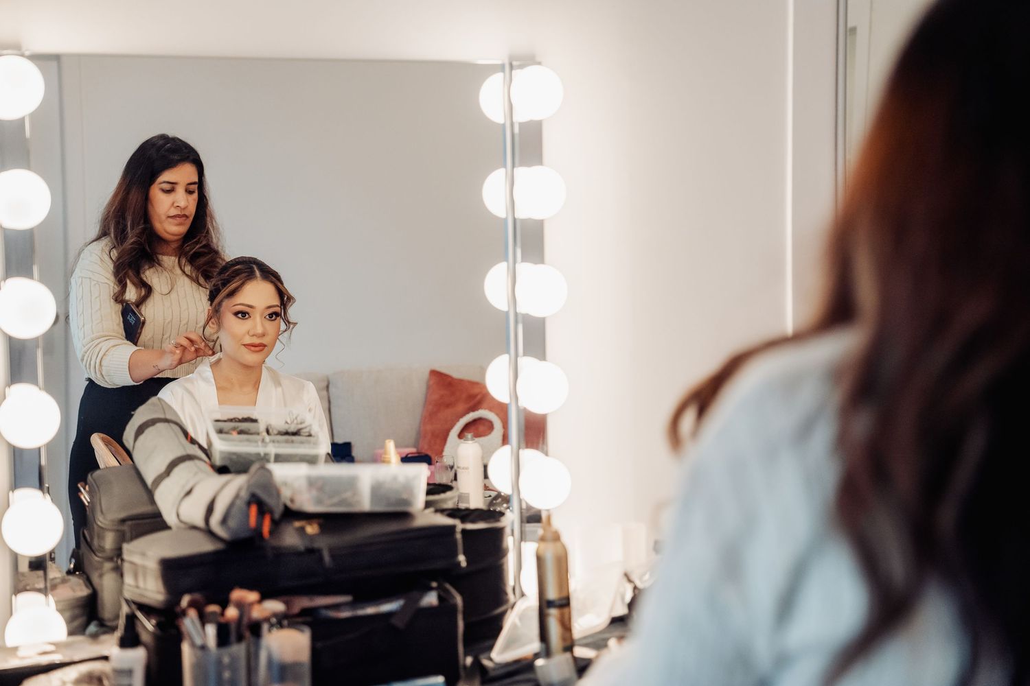 Behind the scenes view of bridal makeup preparations taking place at vanity mirrors with bright lighting.