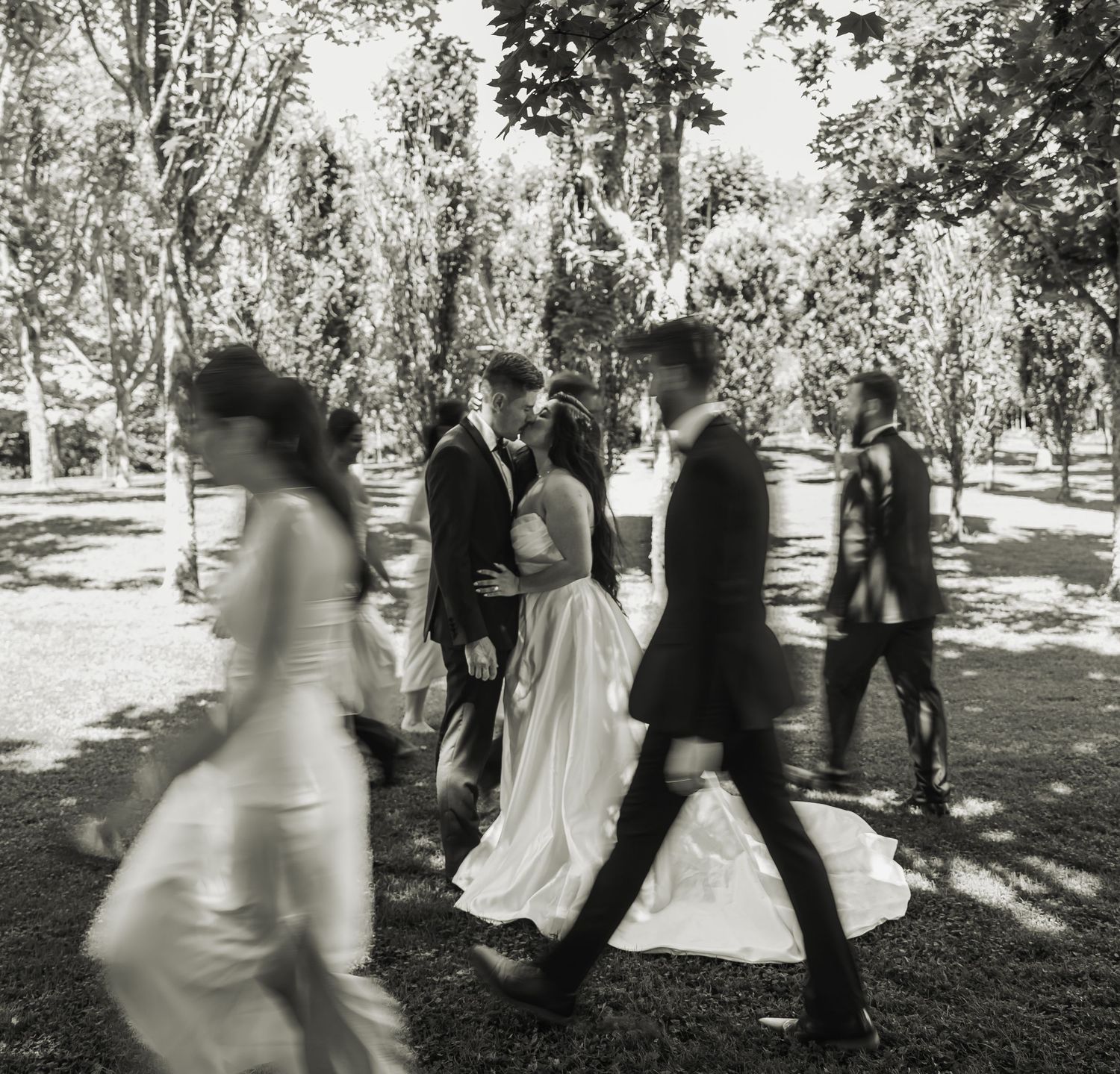Black and white photo of wedding party walking past embracing bride and groom.