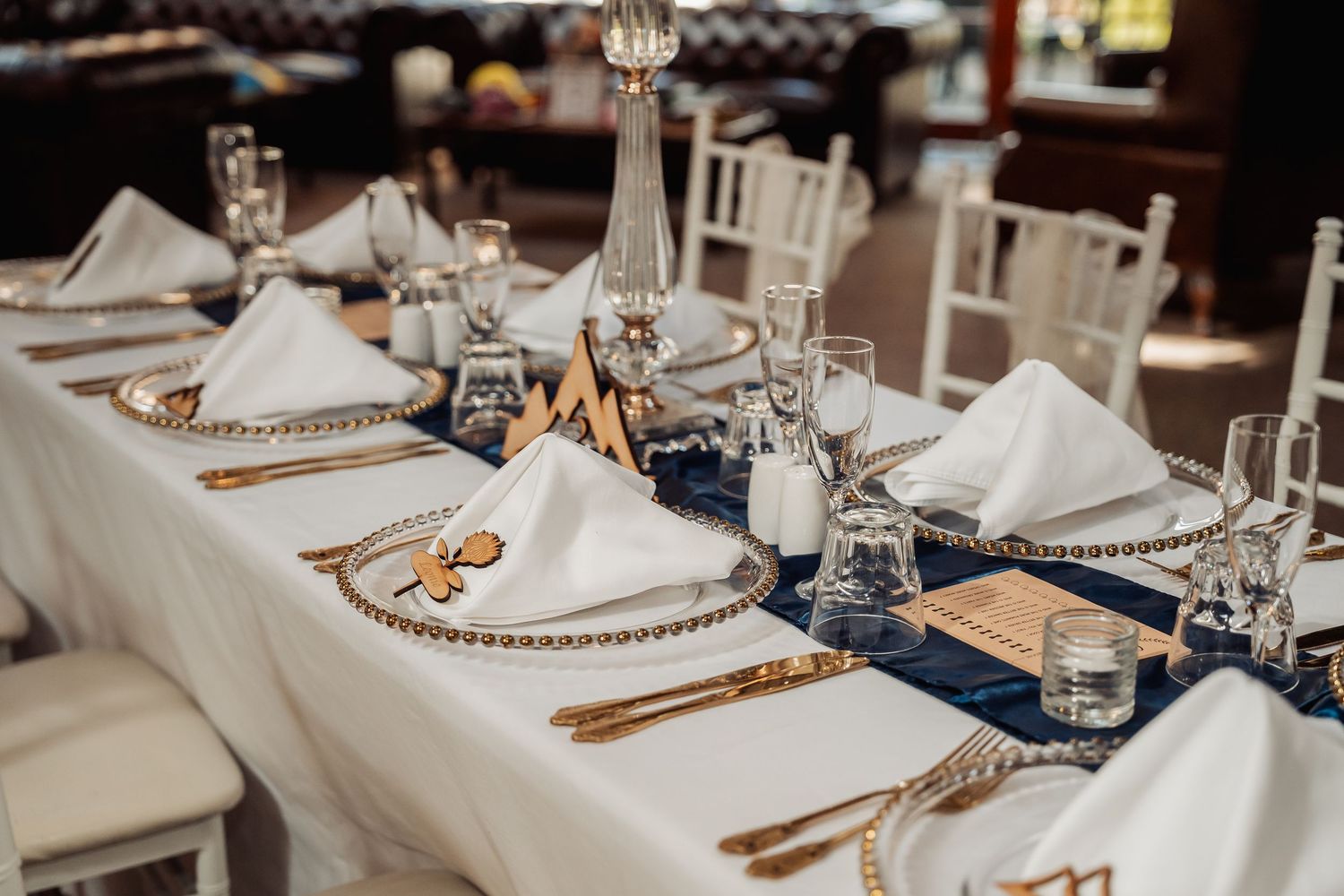 An elegant wedding table setting with white linens, gold charger plates, and crystal glassware.