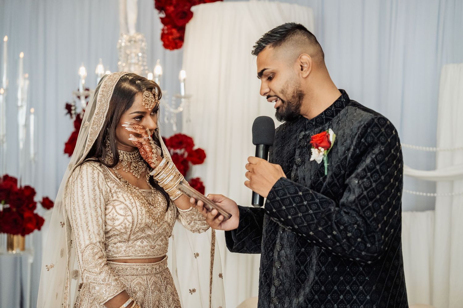 Romantic couple shares intimate moments in formal attire against white drapes with red floral accents.