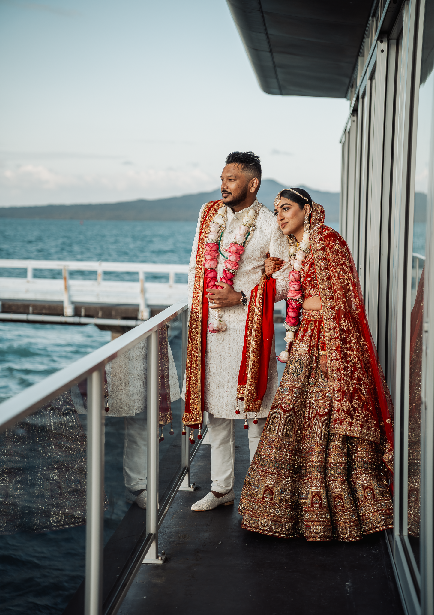 Wedding couple in traditional Indian formal wear standing on seaside balcony.