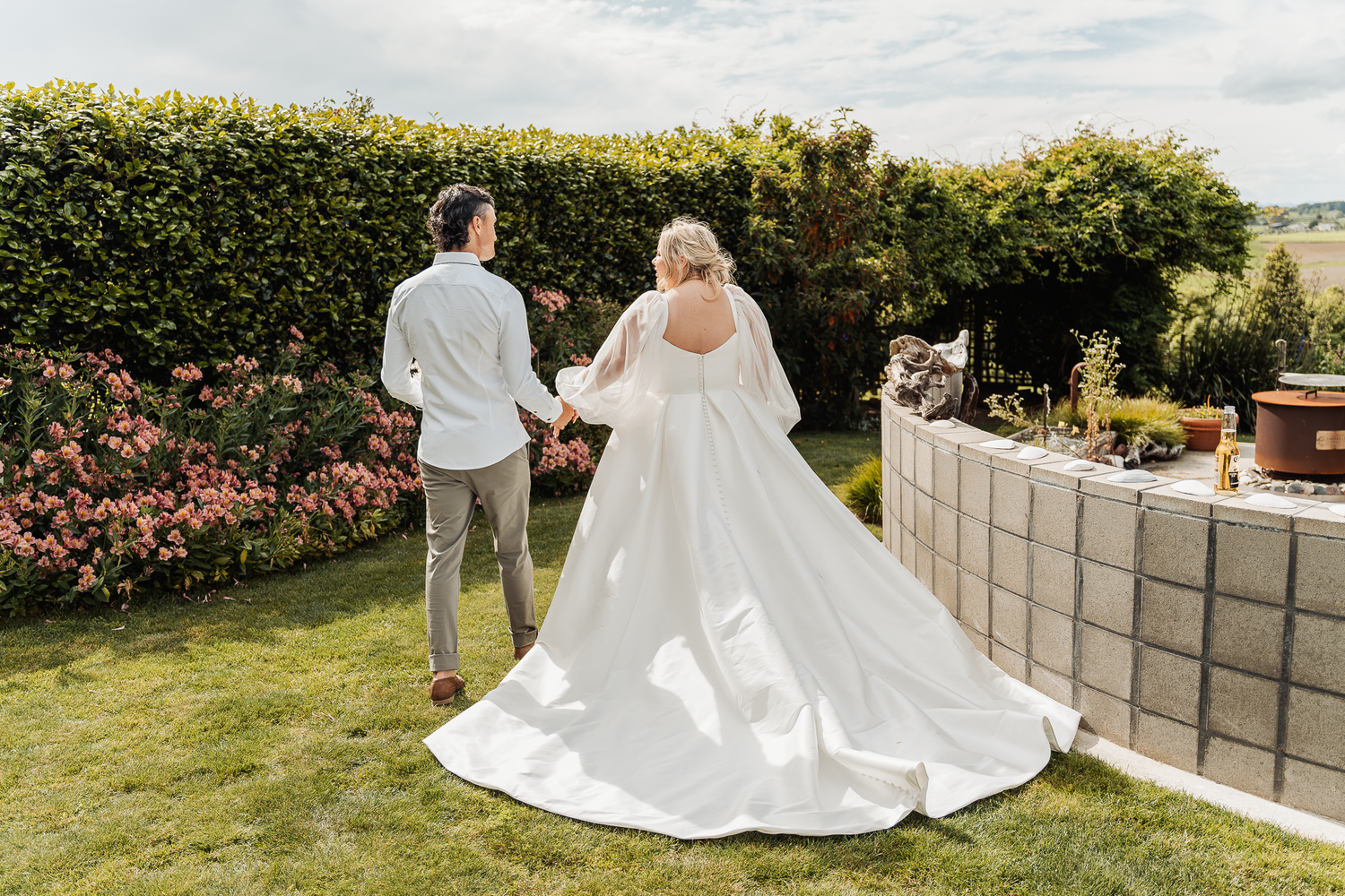 Couple walking on manicured lawn with bride wearing flowing white dress with long train.