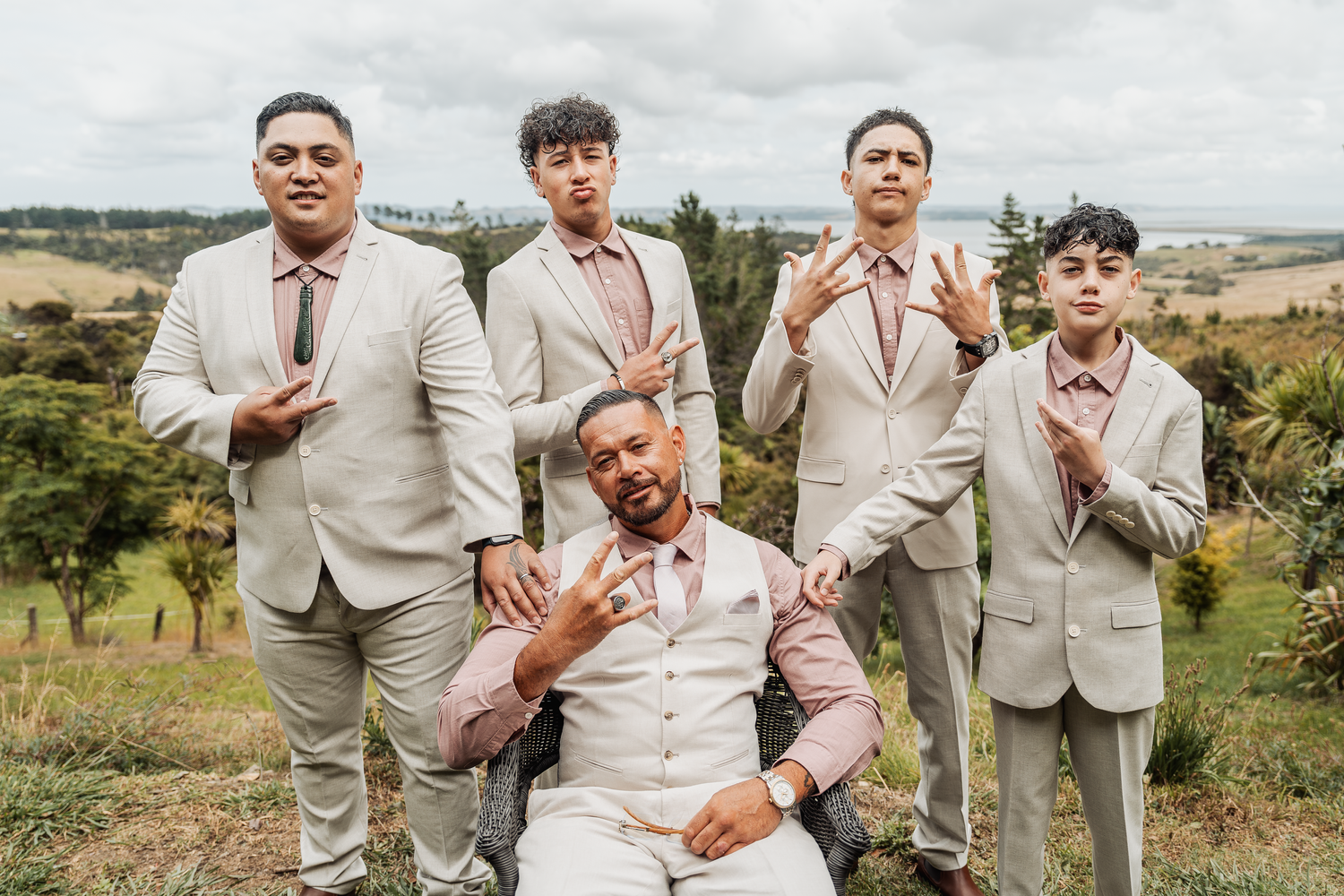 Groomsmen in matching beige suits pose in countryside setting.
