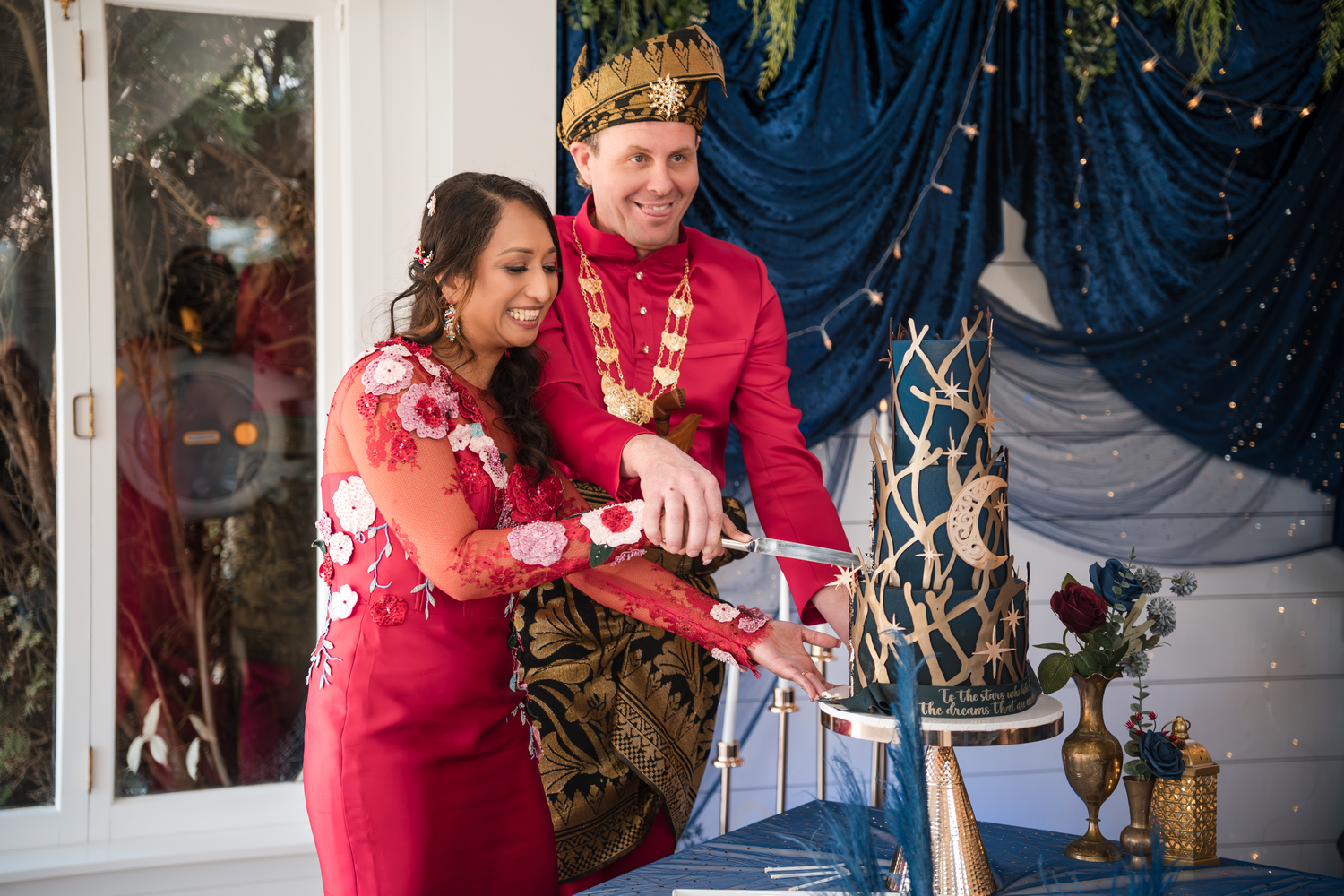 Couple in coordinating red formal wear performs traditional cake cutting ceremony.