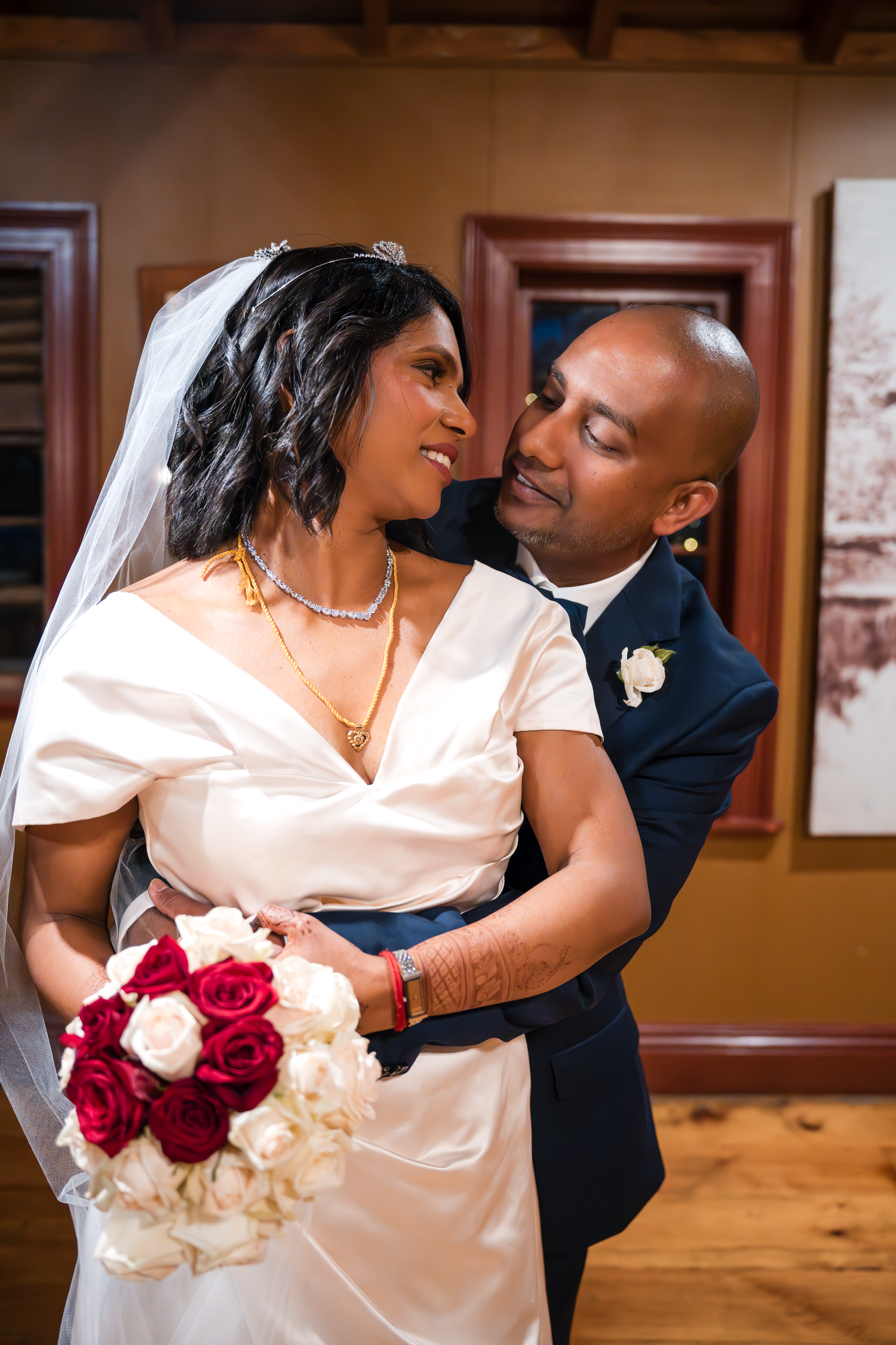 A romantic wedding portrait shows a couple embracing while holding a bouquet of roses.