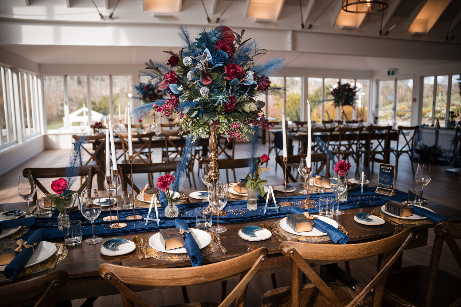 Wedding reception table with blue place settings and dramatic floral centerpieces.