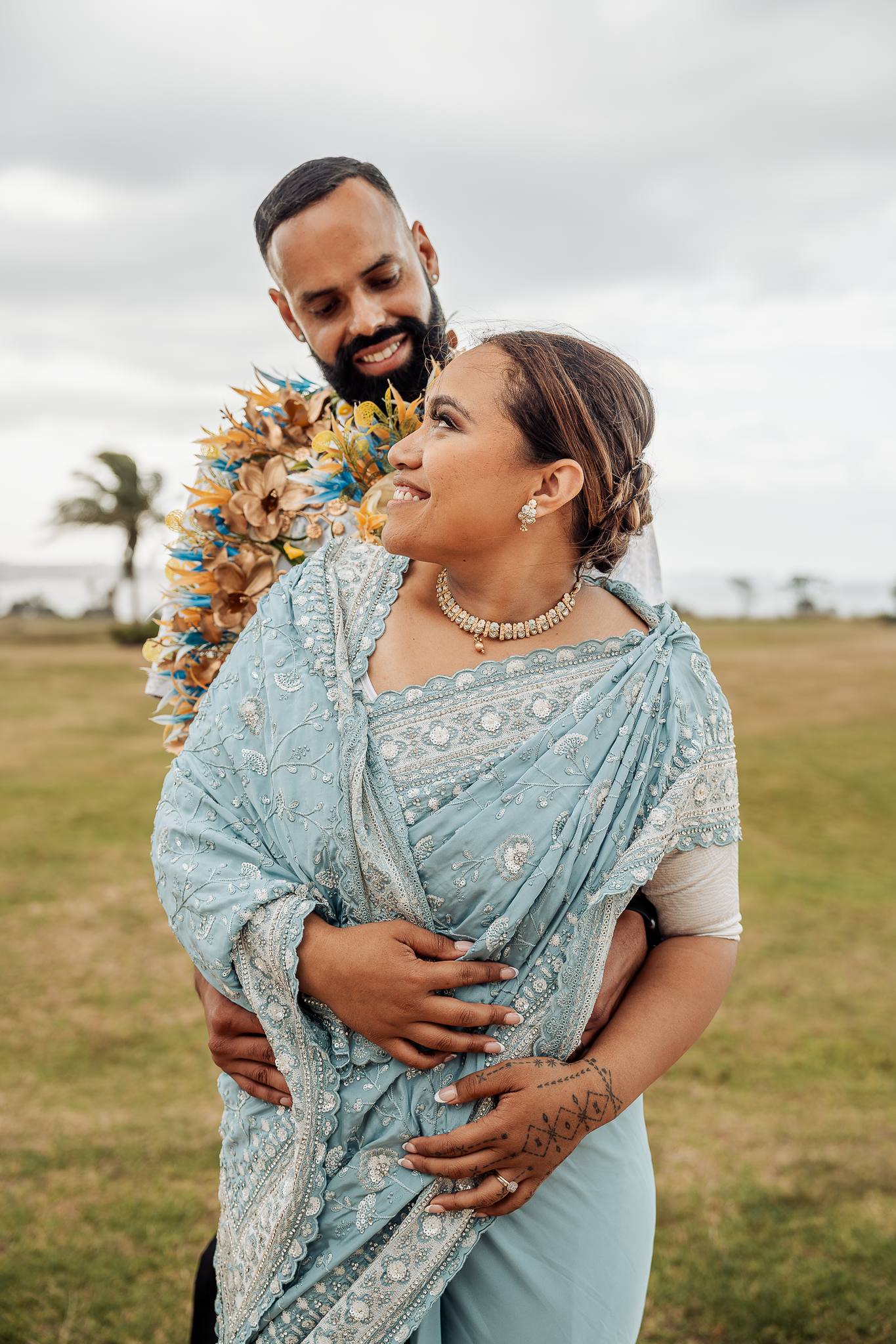 Couple in traditional dress shares tender moment against grassy landscape.