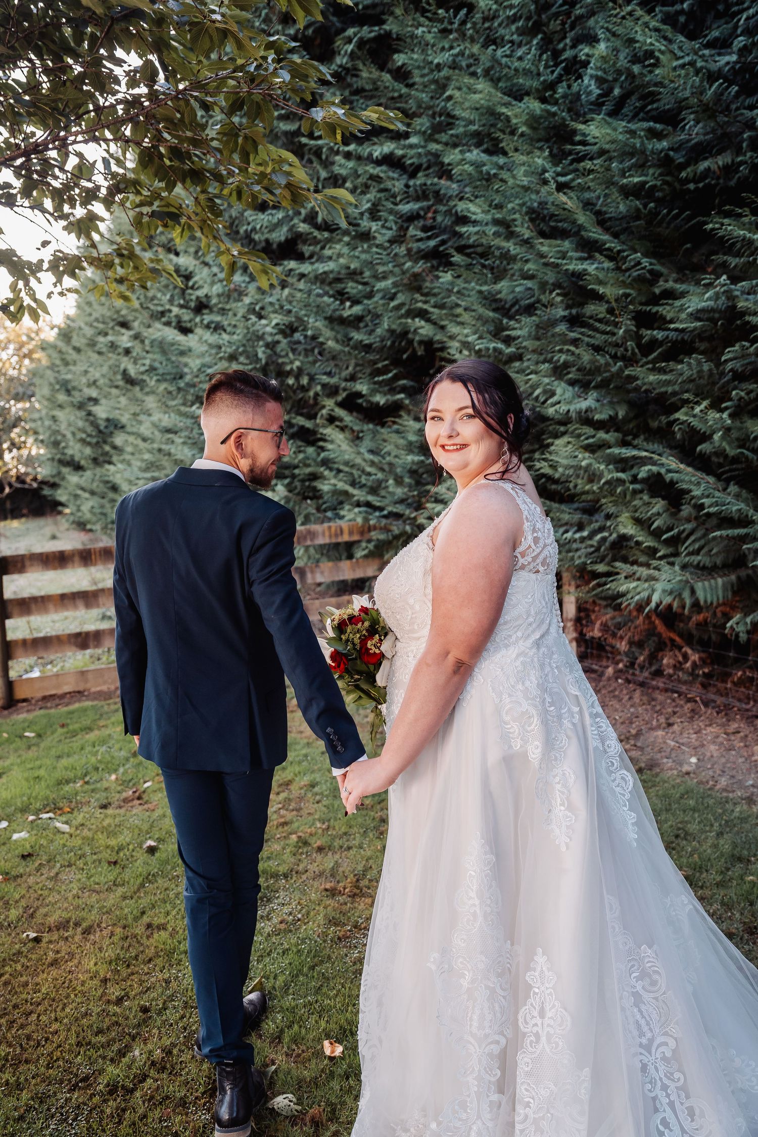 A bride in a lace gown and groom in navy suit share a playful moment in a garden setting.