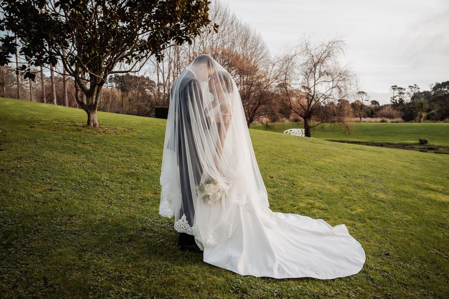 Flowing white wedding dress train trails across a lush green lawn.