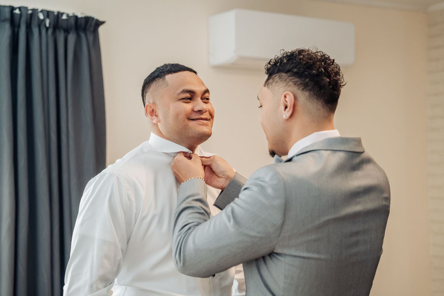 Two well-dressed men in formal attire help adjust a bowtie before a special occasion.