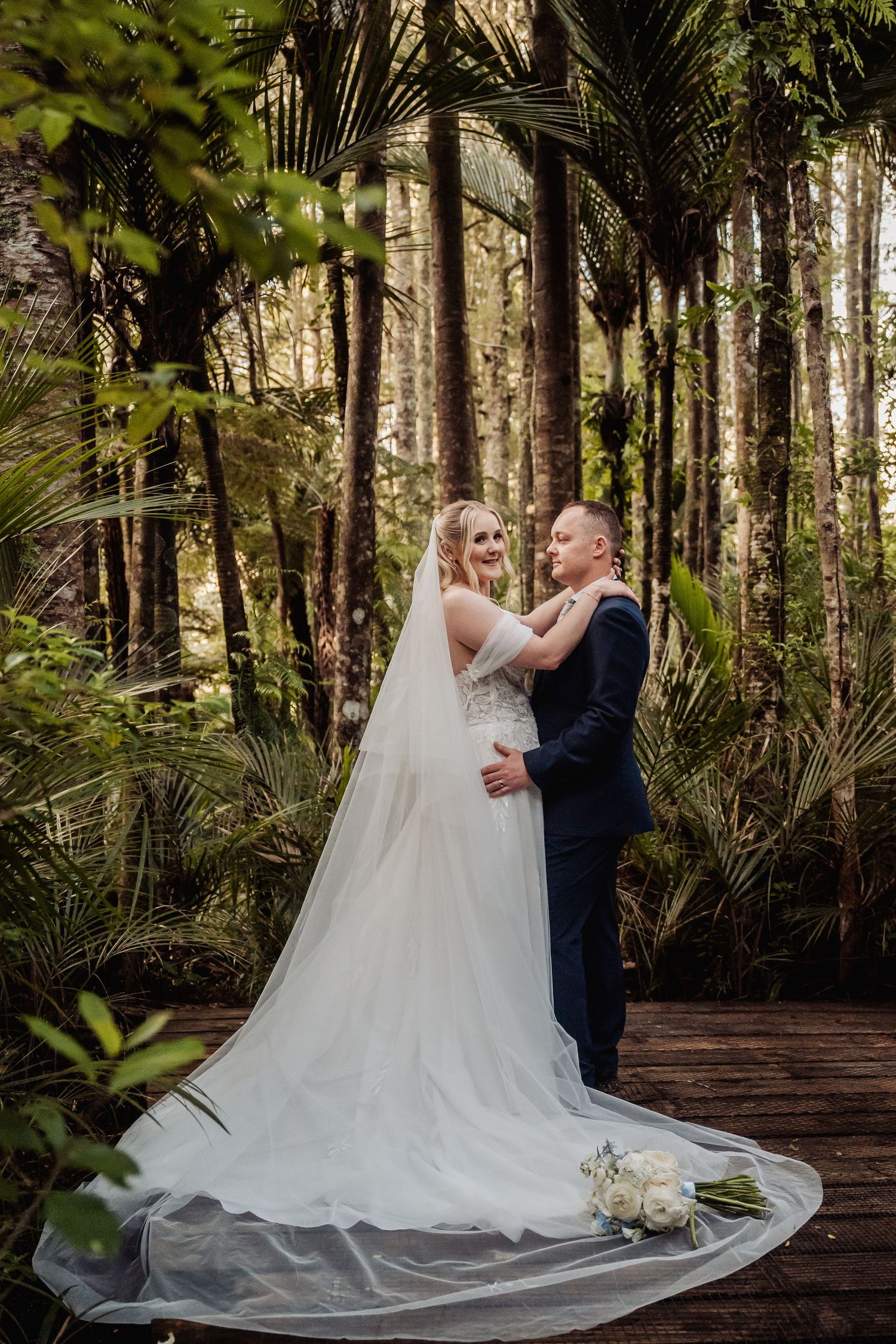 Romantic wedding portraits on a wooden walkway surrounded by lush tropical forest.