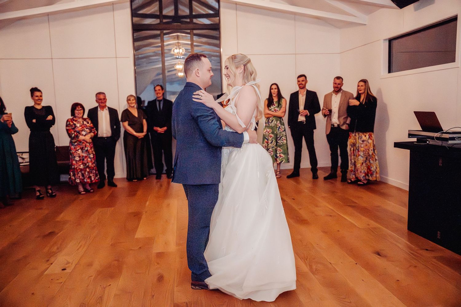 Wedding reception venue with wooden floors and exposed beam ceiling during couple's dance.